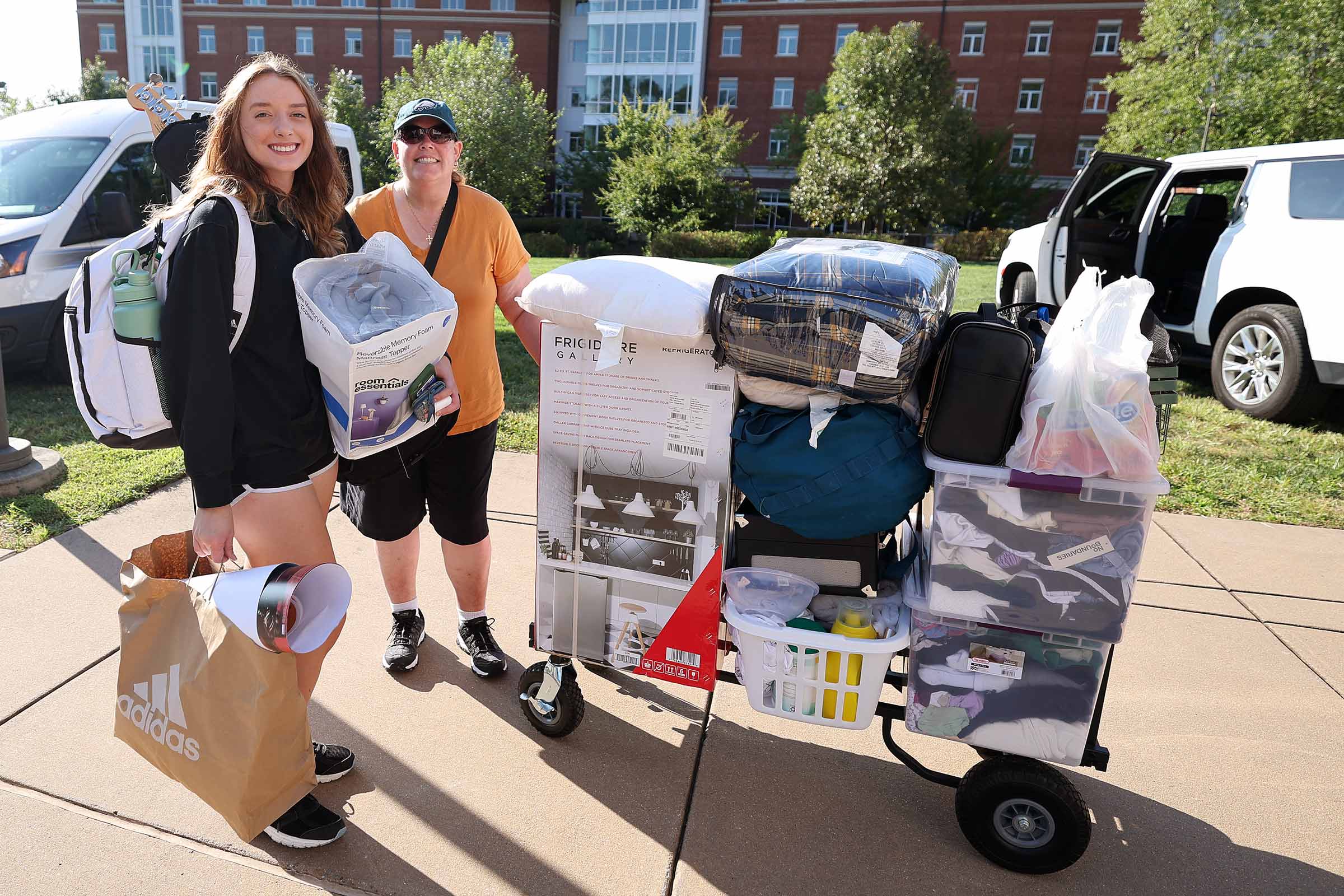 A student and parent stop and smile for the camera next to their cart stacked high with boxes