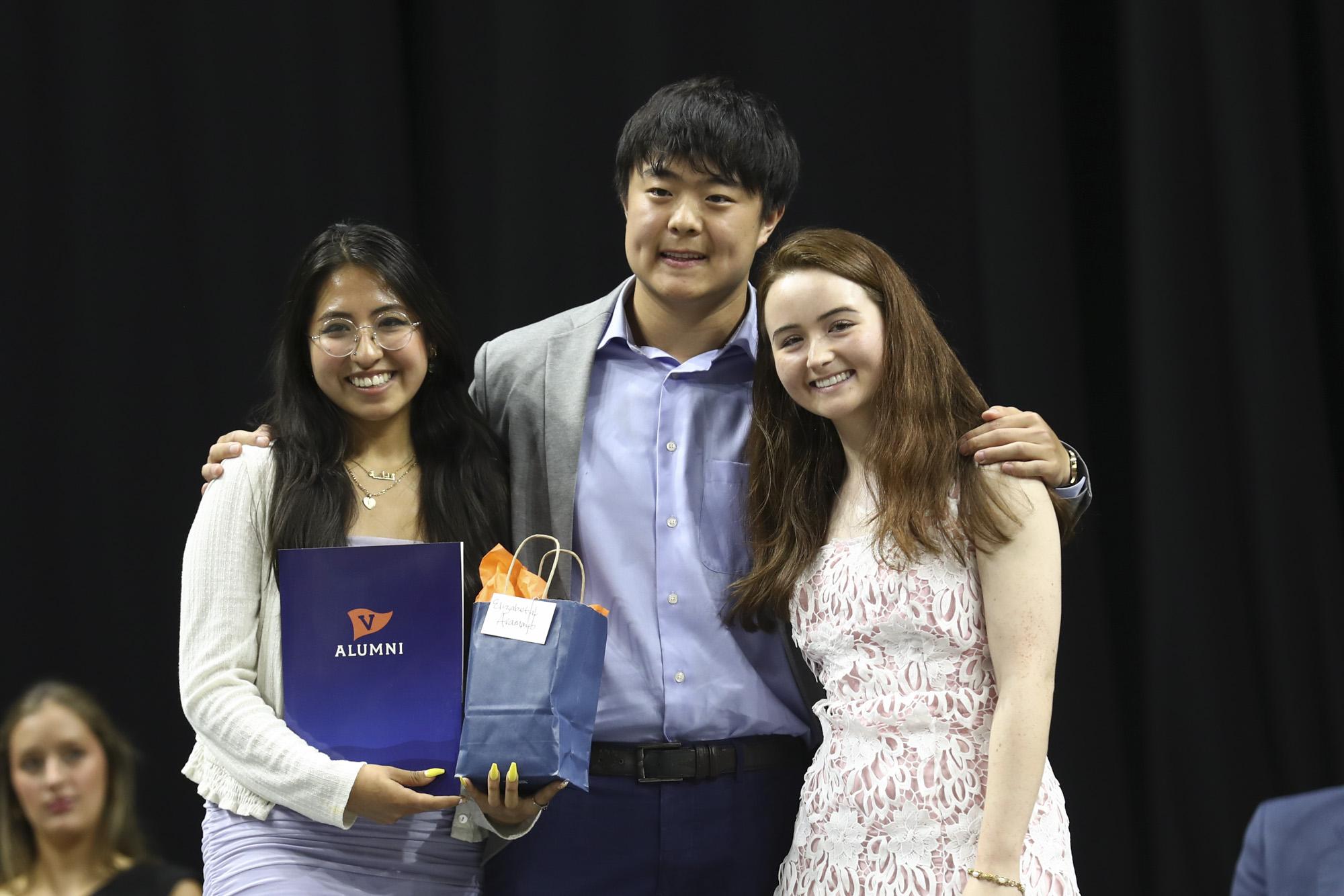 A smiling woman holding a gift bag poses for a photo with a man and a woman