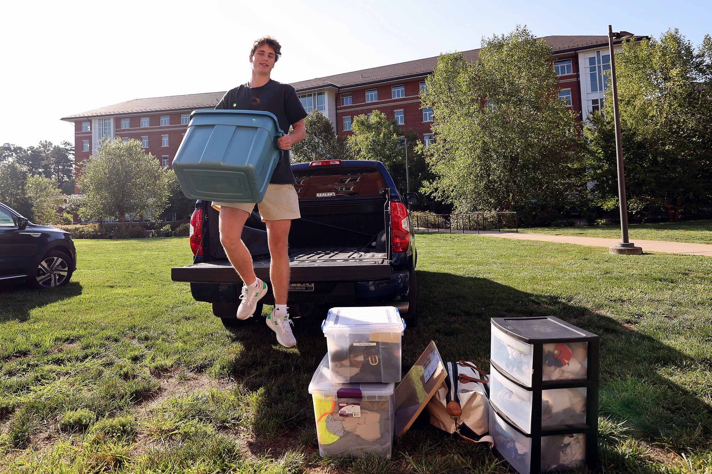 A student jumps off the bed of a truck with a box to add to the pile to go inside a dorm