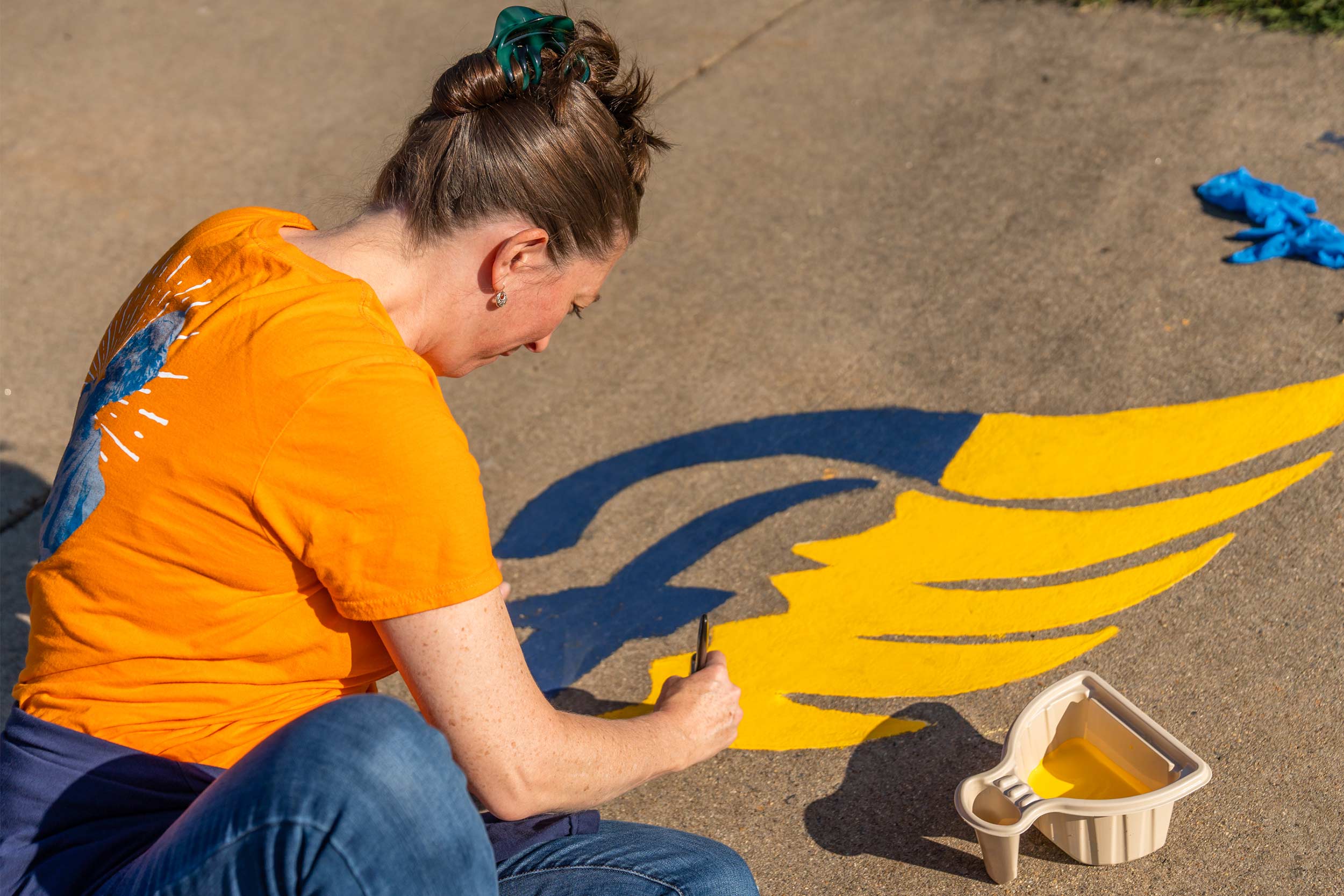 A woman touches up a faded high-school logo. 