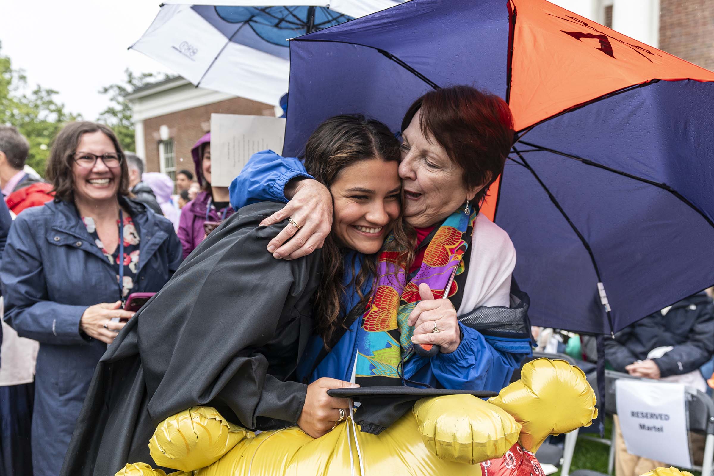 Student with loved one embracing excitedly with balloons under an orange and blue Virginia umbrella