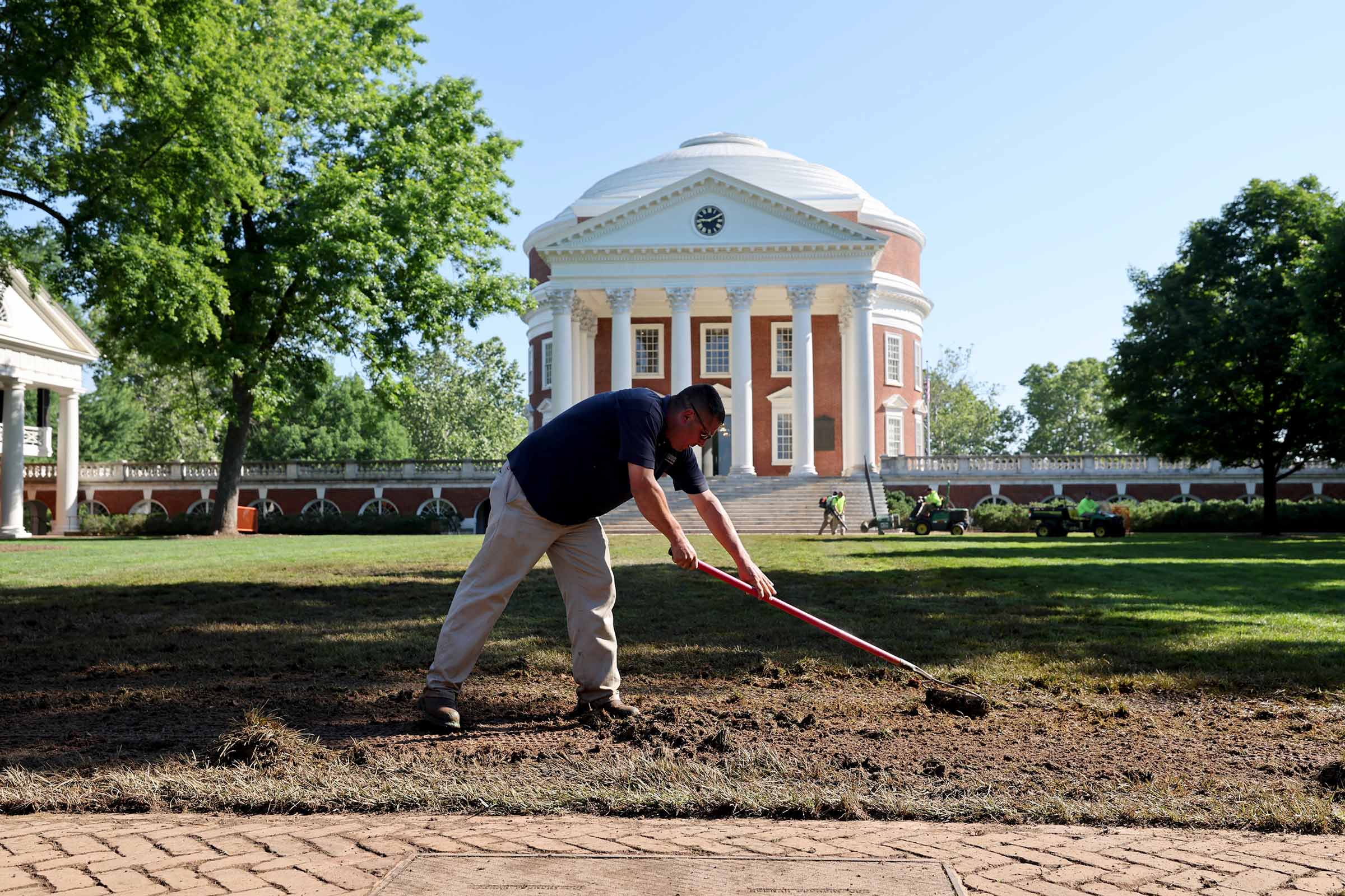 Turf supervisor Jonathan Racey uses a rake to remove mulch from mud in the work to restore the Lawn after Finals Weekend. 