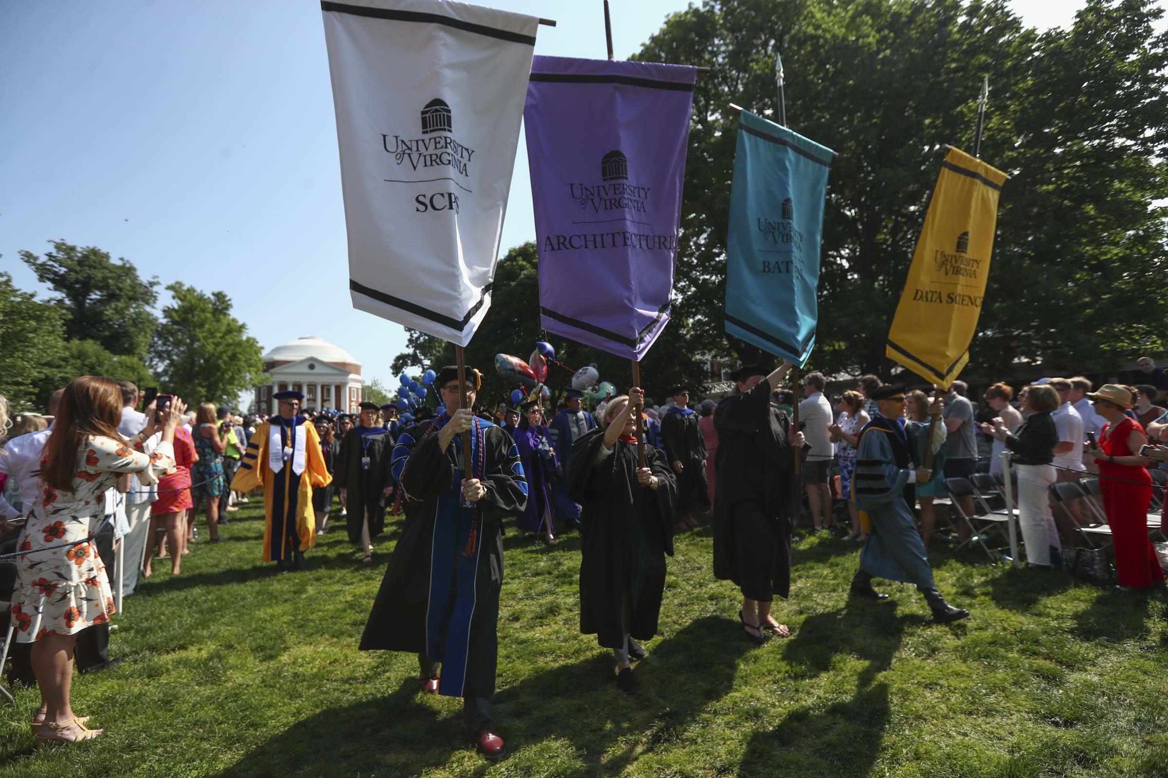Standard-bearers hoisting the banners of four University schools lead their graduates across the Lawn.