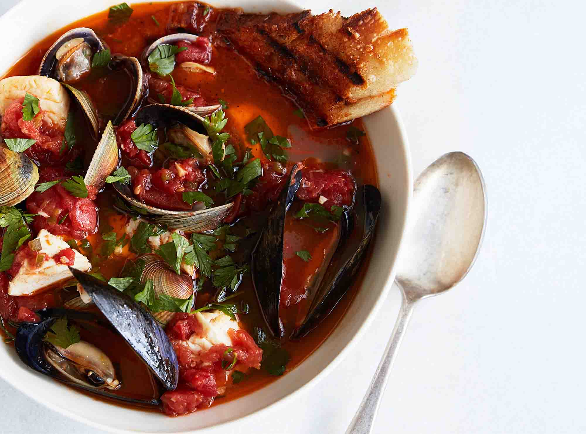 Mussles and good crusty bread popping out of a hearty seafood and tomato soup