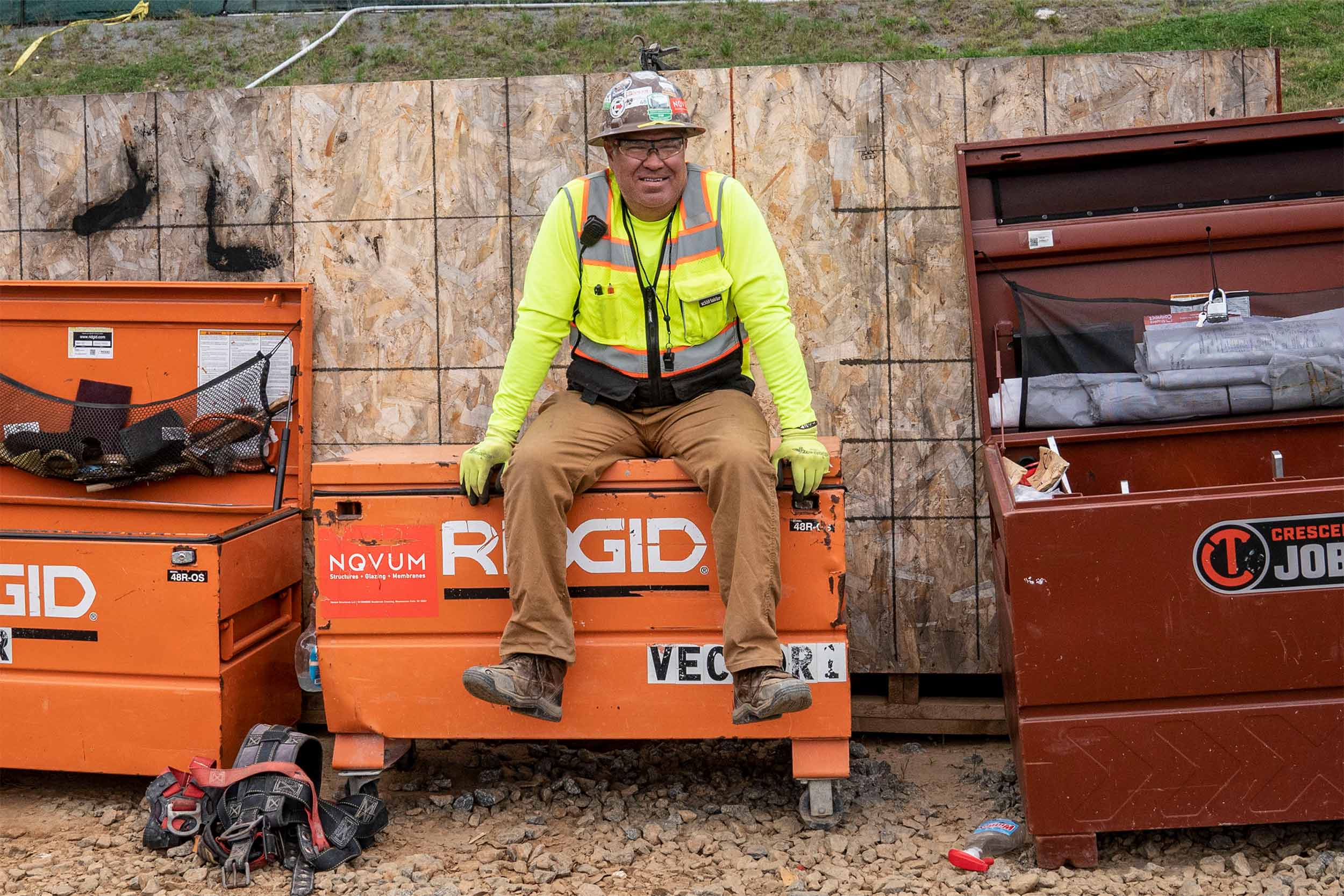 A worker sits on a large, orange toolbox in front of a sheet of OSB