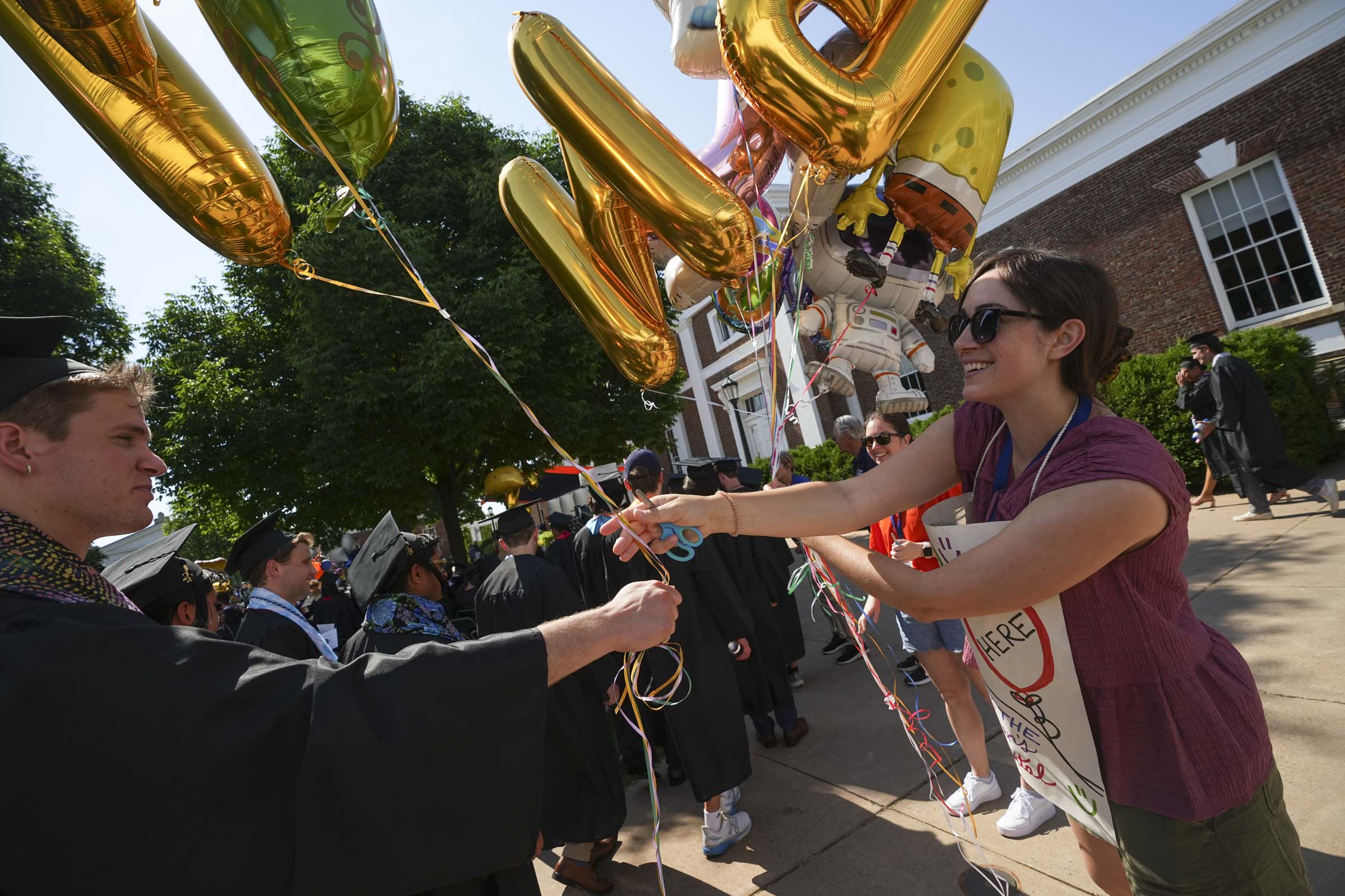 A woman wearing a sign accepts balloons from a student in the crowd.