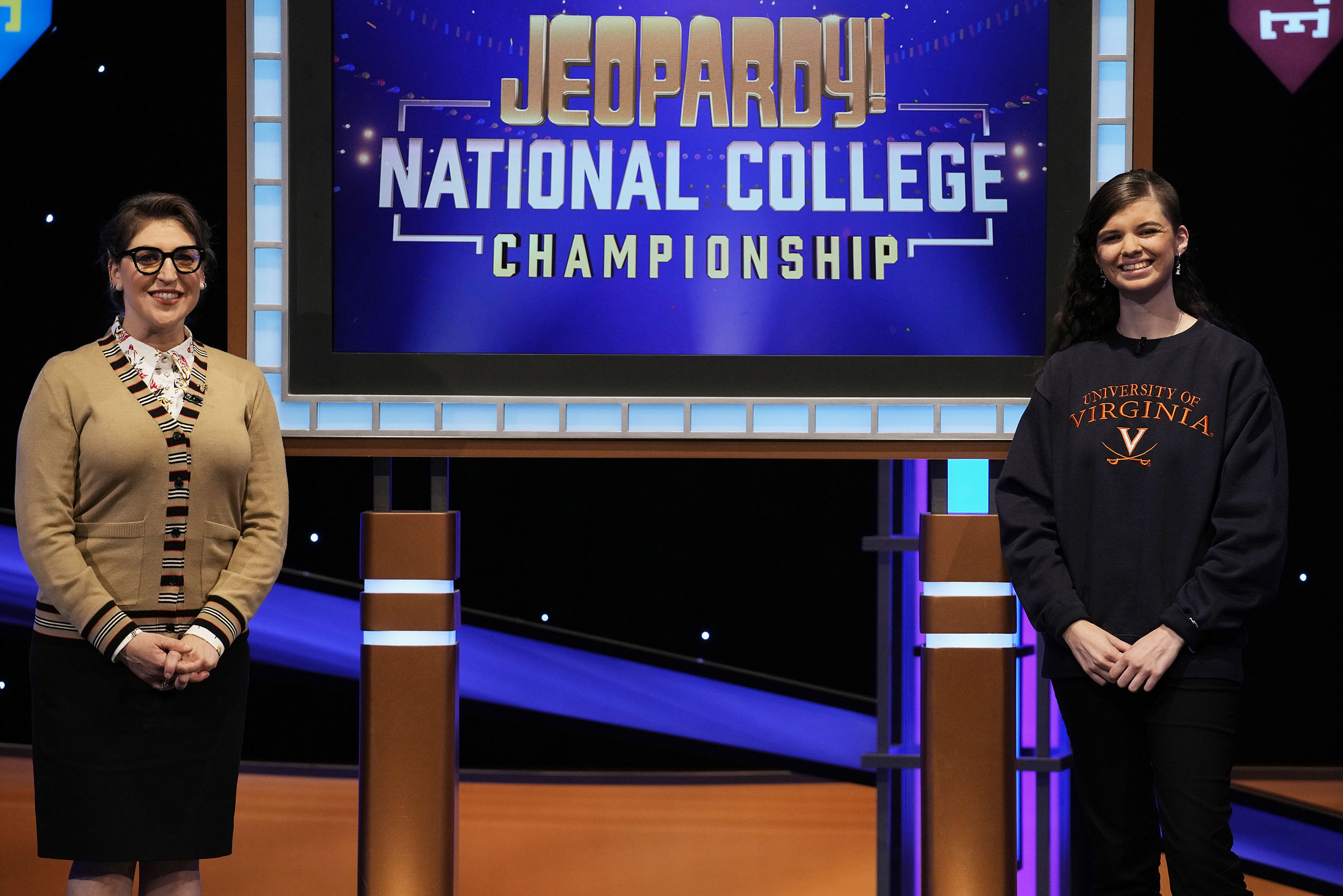 Mayim Bialik on the left and Megan Sullivan on the right with a screen in the middle that reads Jeopardy! National College Championship