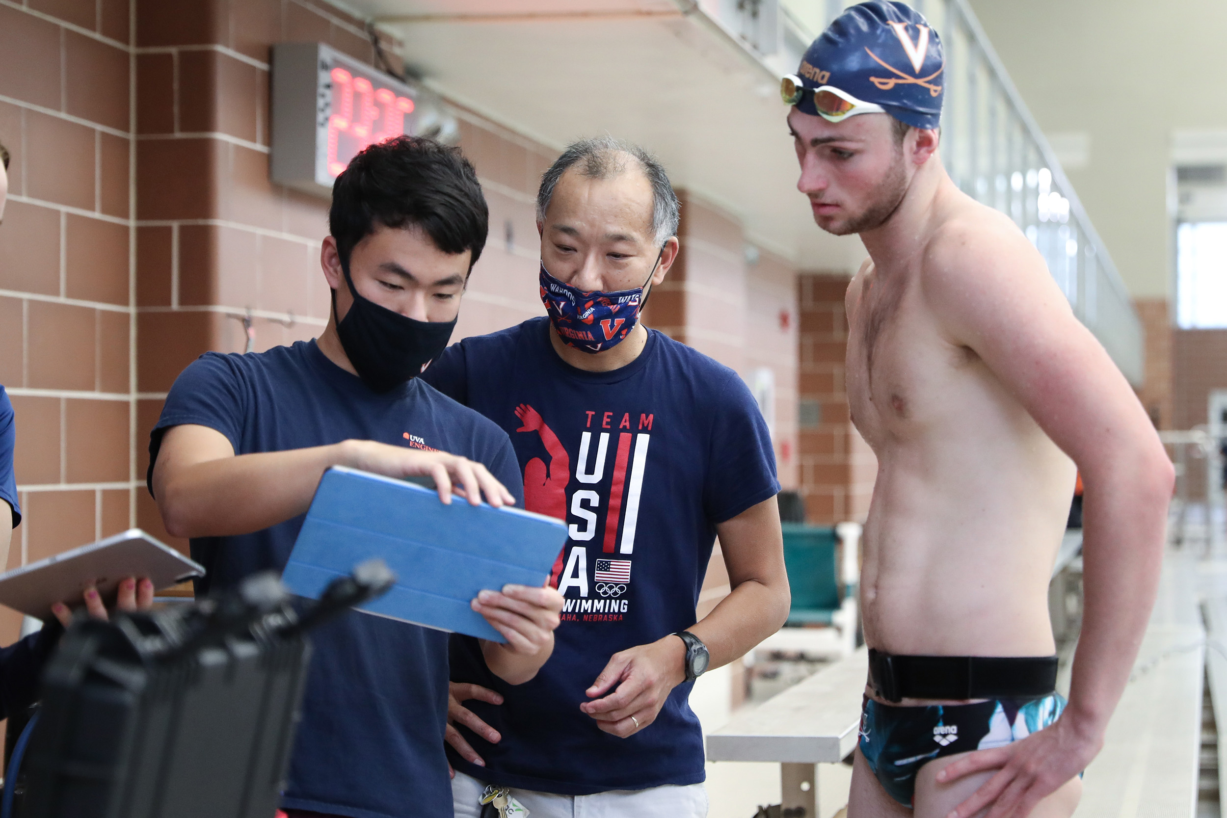Coaches and swimmer looking on tablet at information