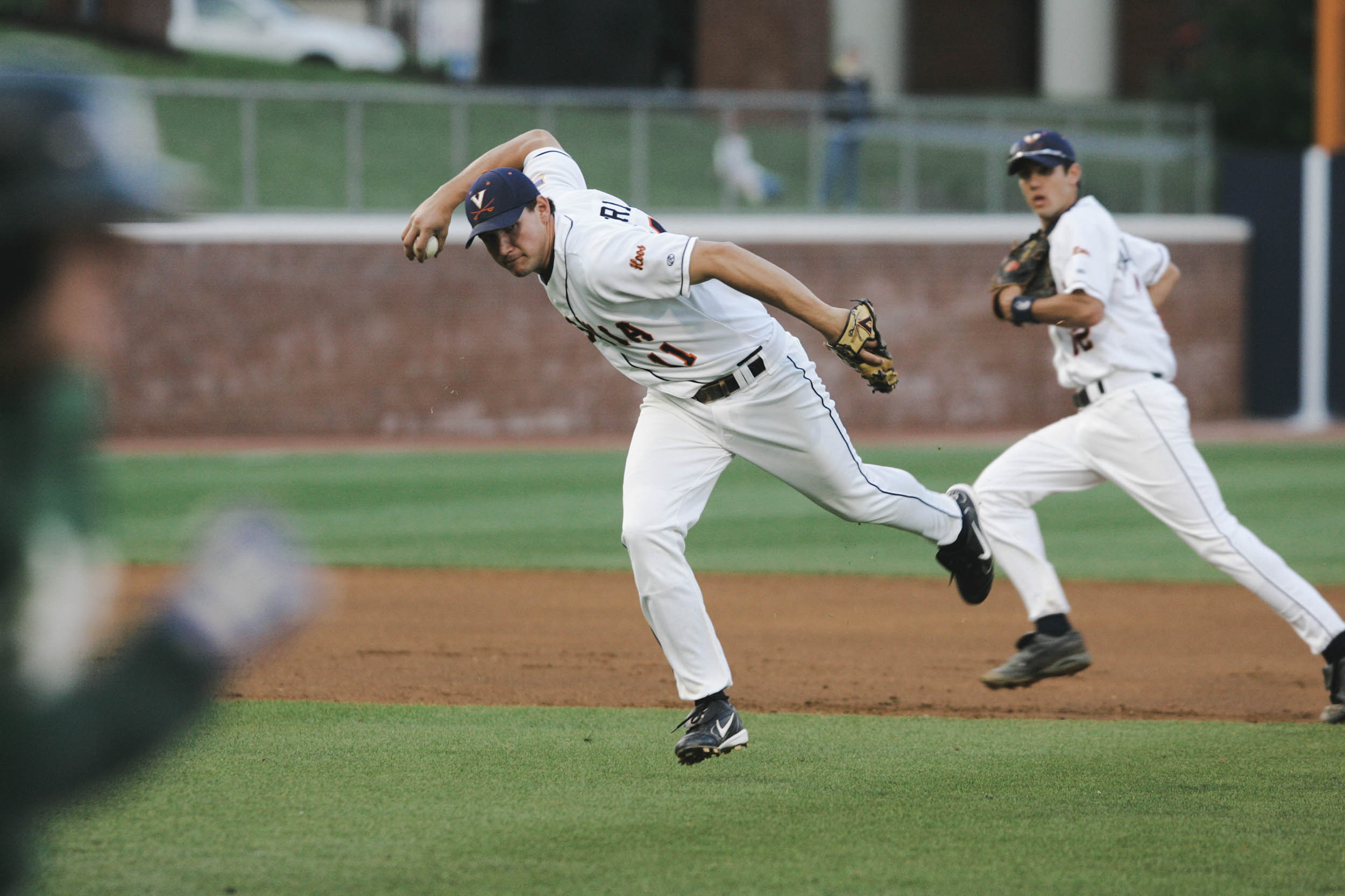 UVA baseball pitcher pitching a ball and an in fielder running