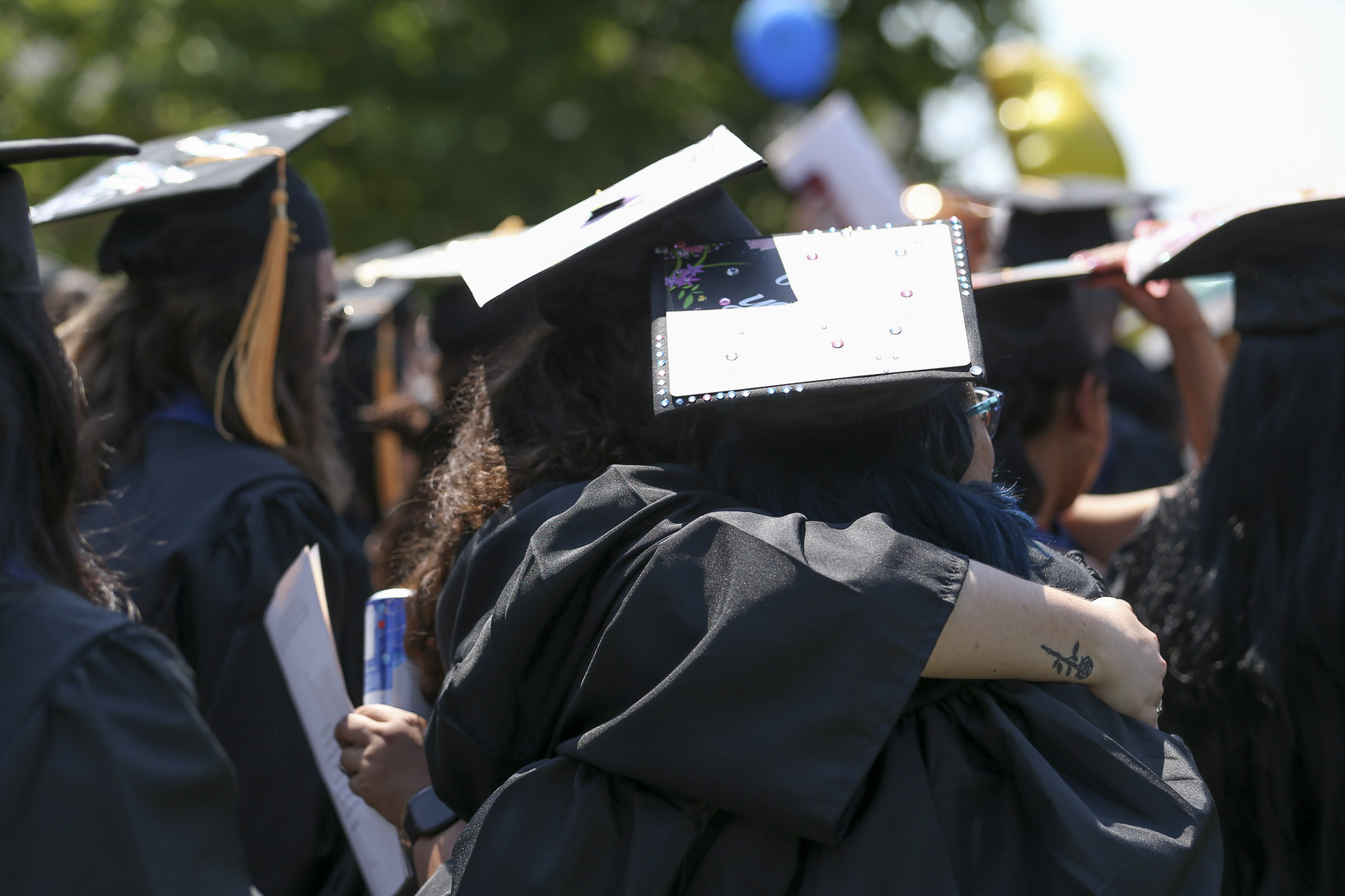 Two students hold each other in a tight embrace as their mortar boards catch the bright sun.