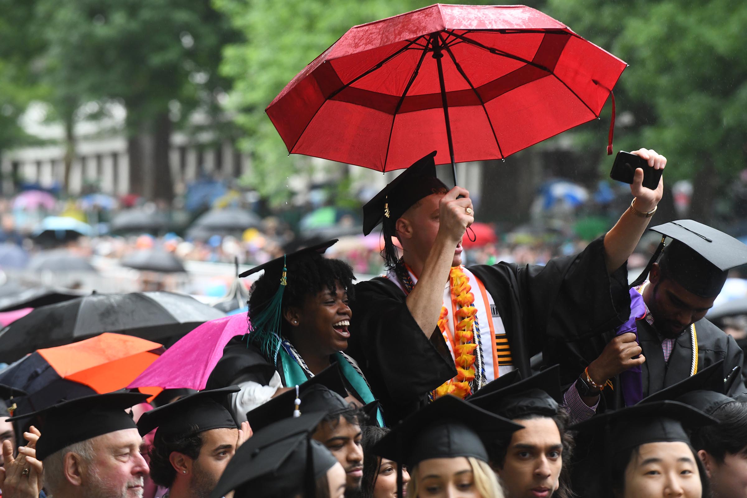 Graduates taking cover under an umbrella during the ceremony