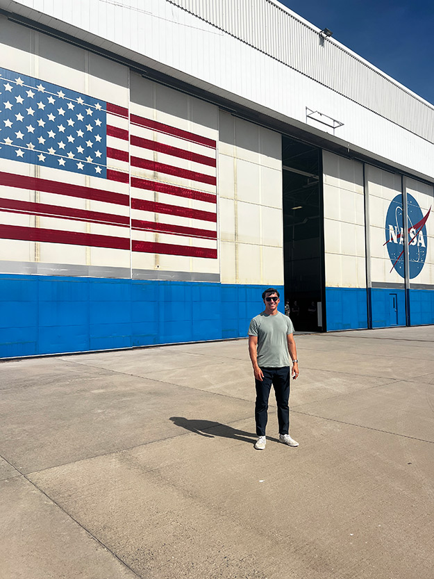 Nicolaas Drapanas standing outside a massive NASA hanger with the US flag painted on it