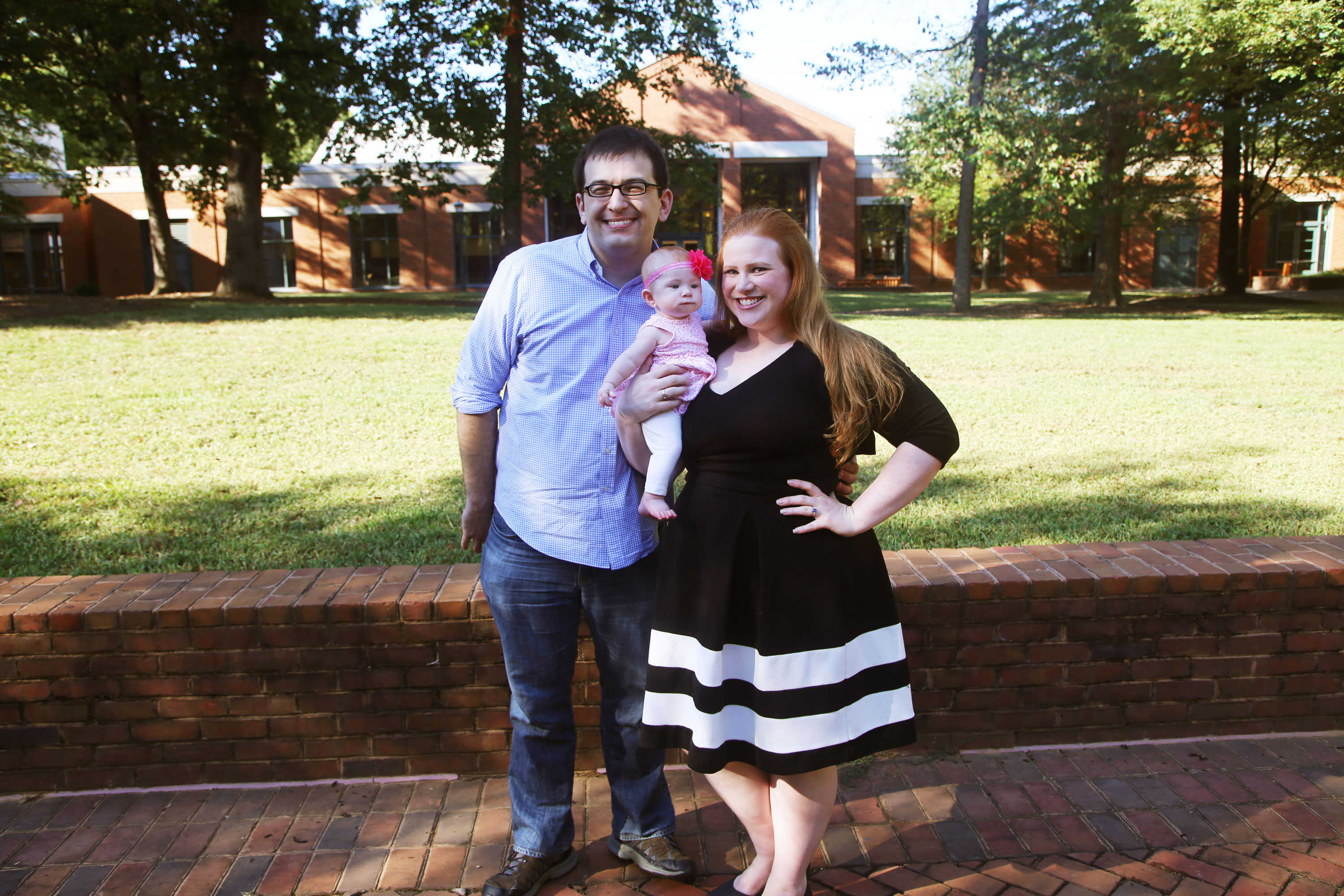 A husband and wife hold their baby outside of a UVA building