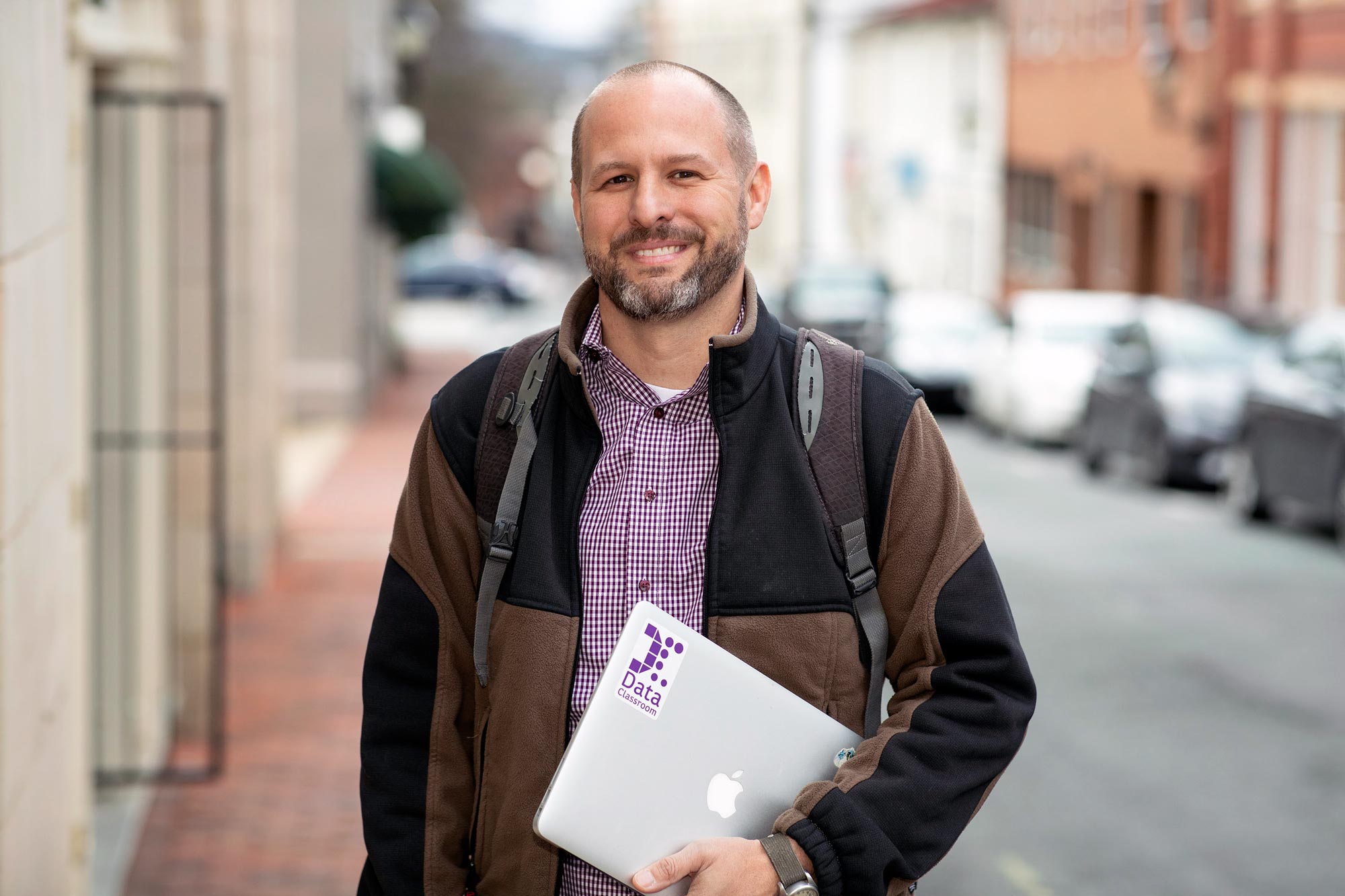 Reedy standing on a sidewalk holding a laptop smiling at camera