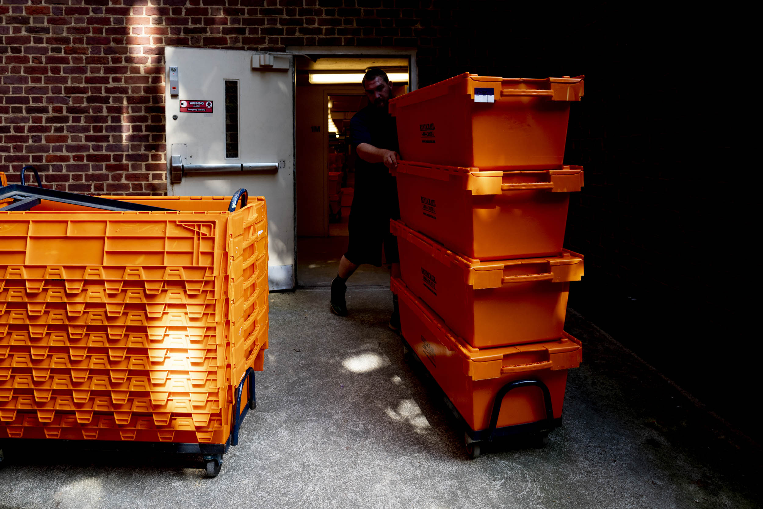 Man moving bright orange boxes out of a building
