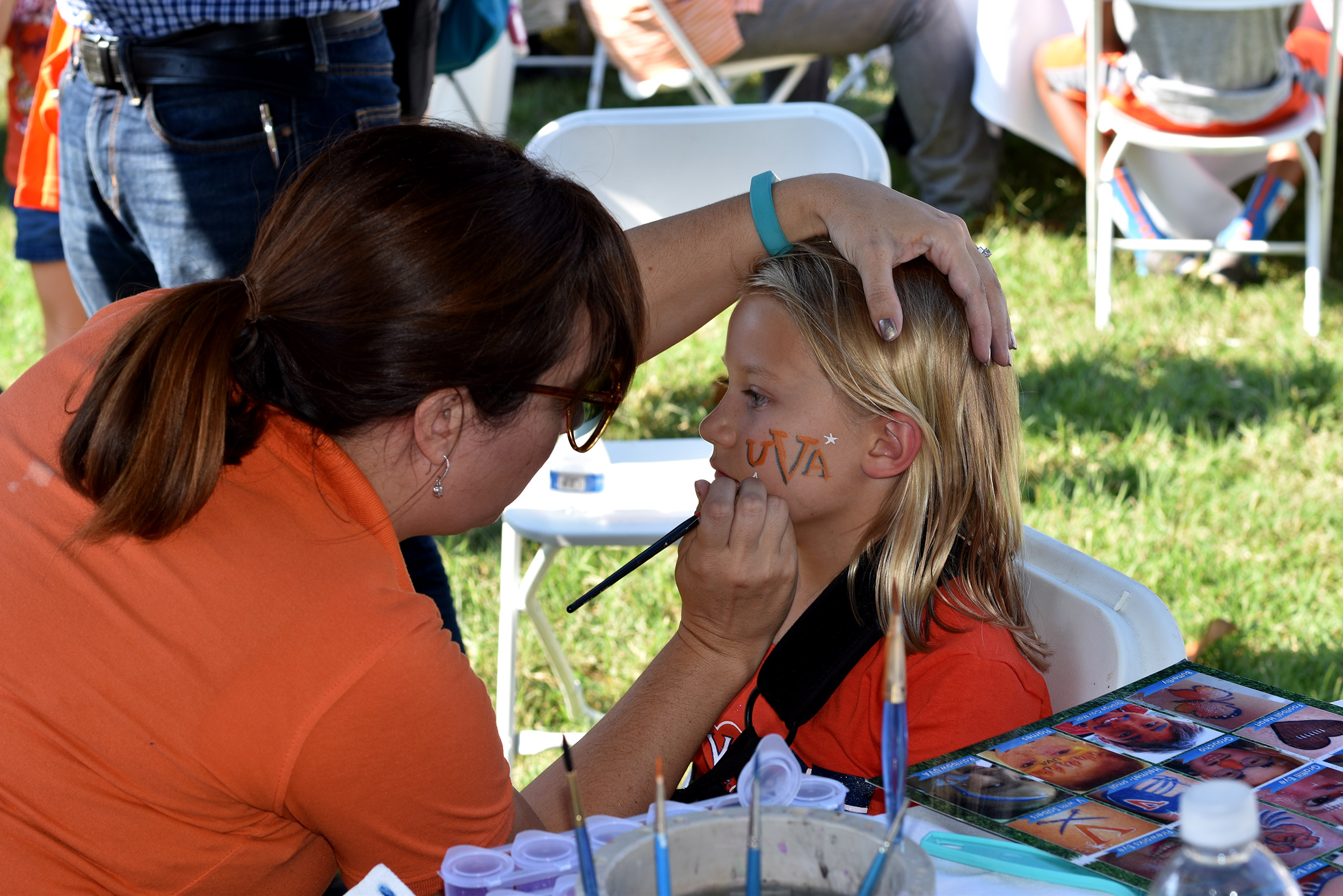 Child having her face painted at a tailgate stateion