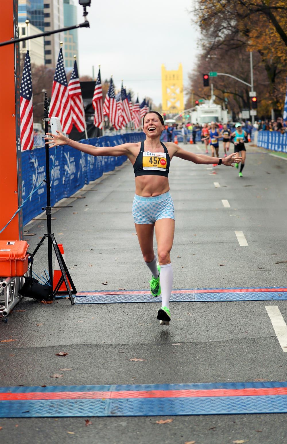 Ann Mazur running across the Olympic Trial marathon finish line with arms stretched out and a huge smile on her face