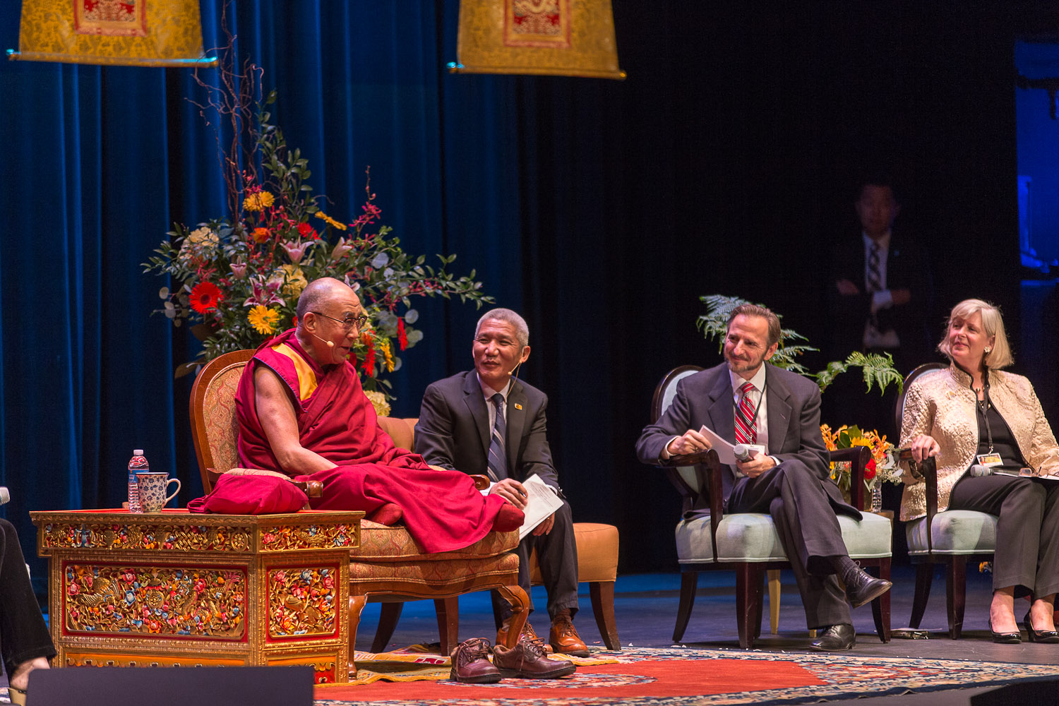 The Dalai Lama  sitting on stage with other panelists during a discussion