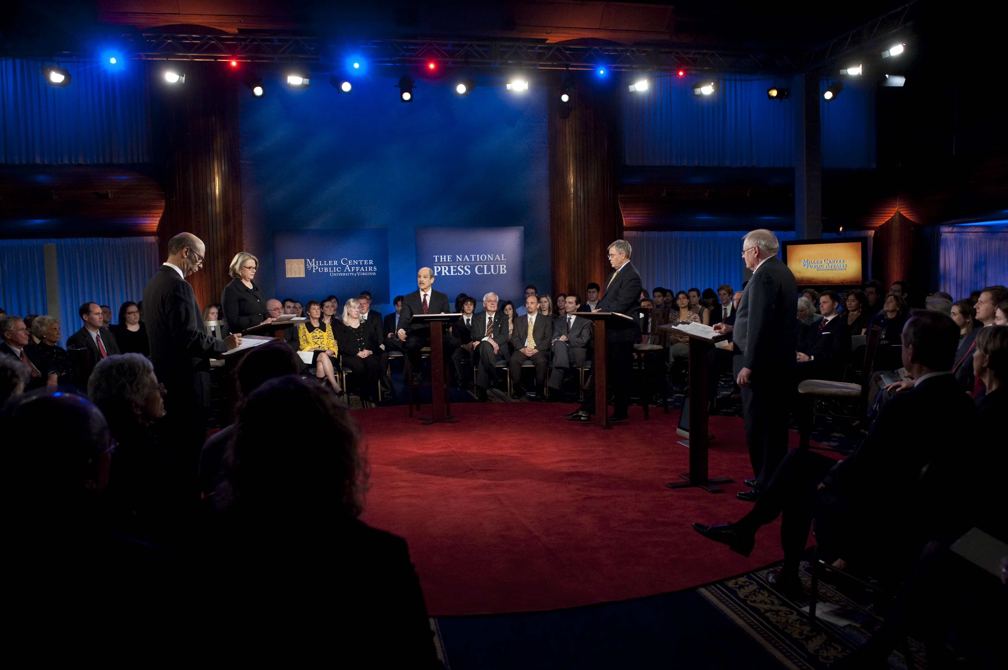 Michael Lomax, Margaret Spellings, Paul Solman, George Leef, and Richard Vedder stand at podiums in a circle during a debate