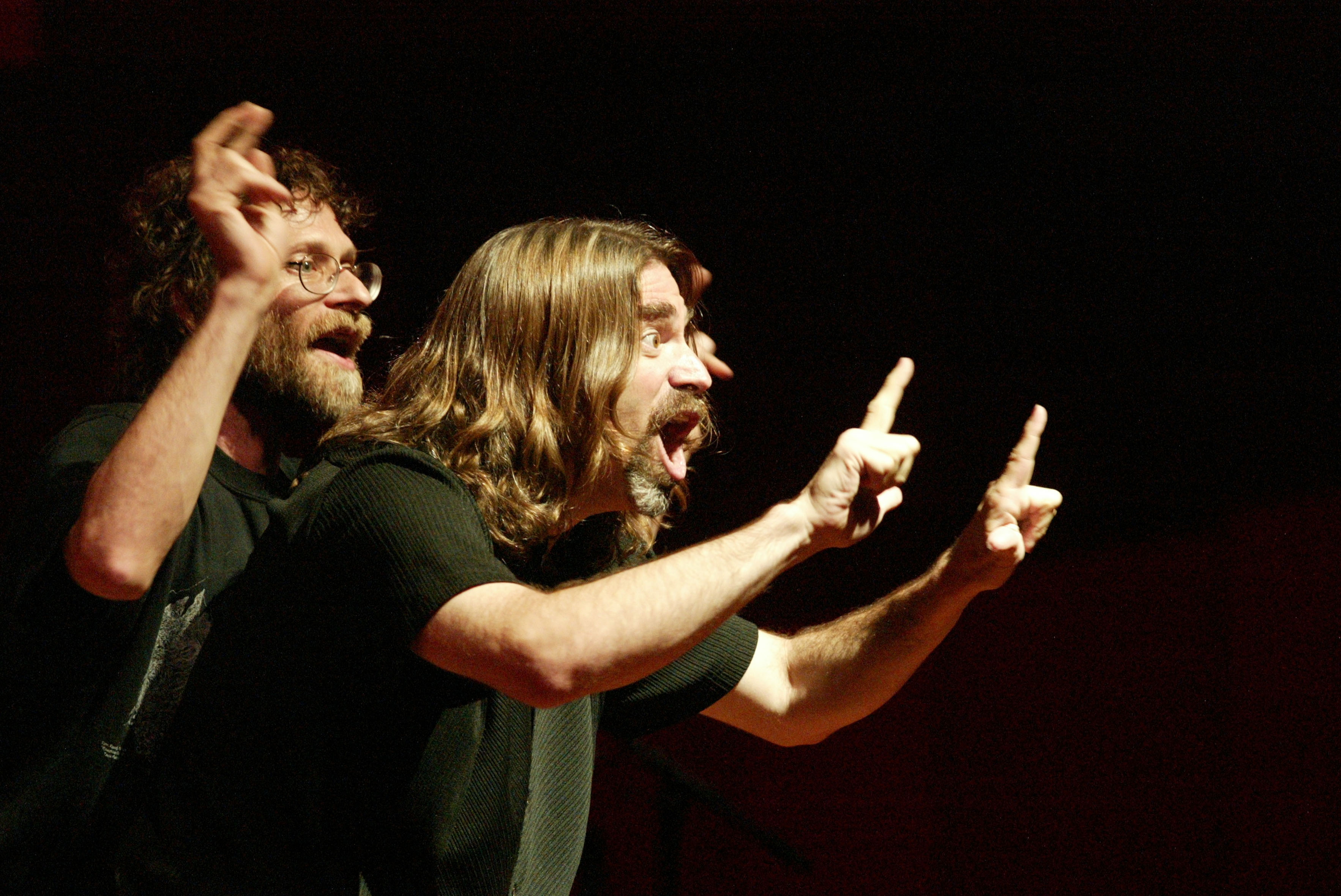 Two men on stage speaking while making hand gestures to the crowd