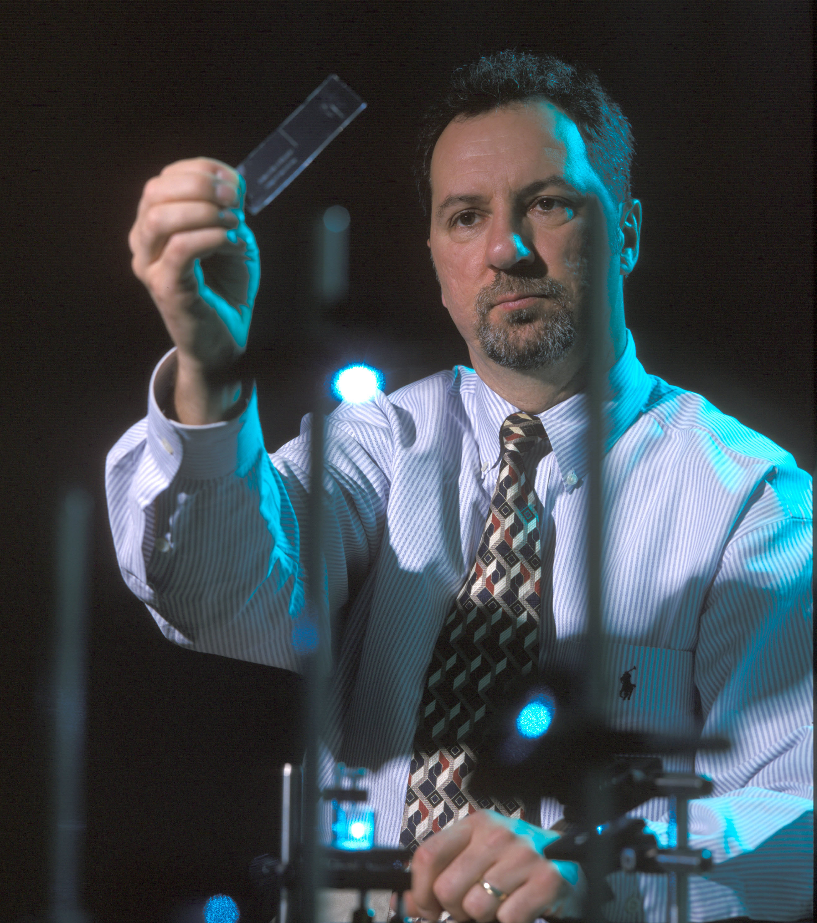 James P. Landers holds up a microscope slide and looks at it