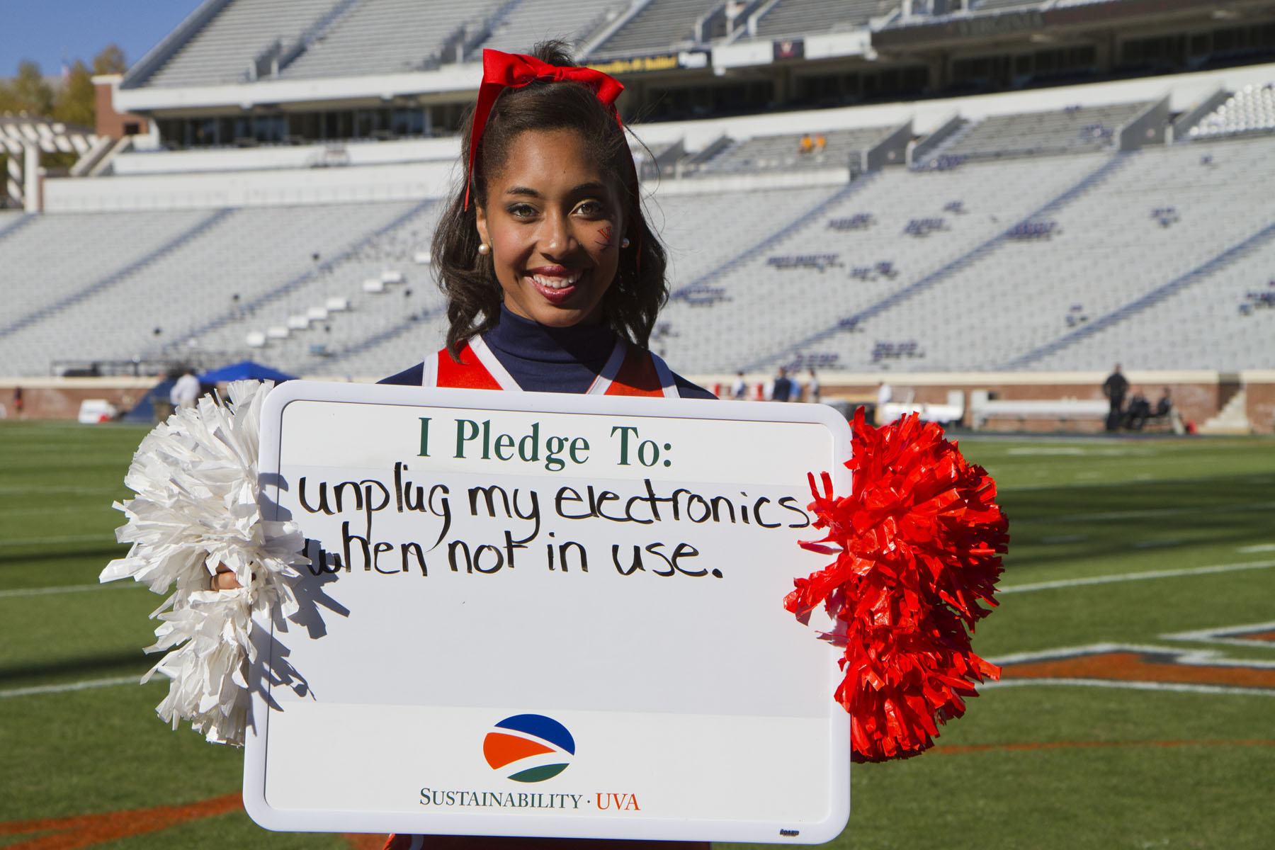 UVA cheerleader holding a sign that reads: I pledge to unplug my electronics when not in use.