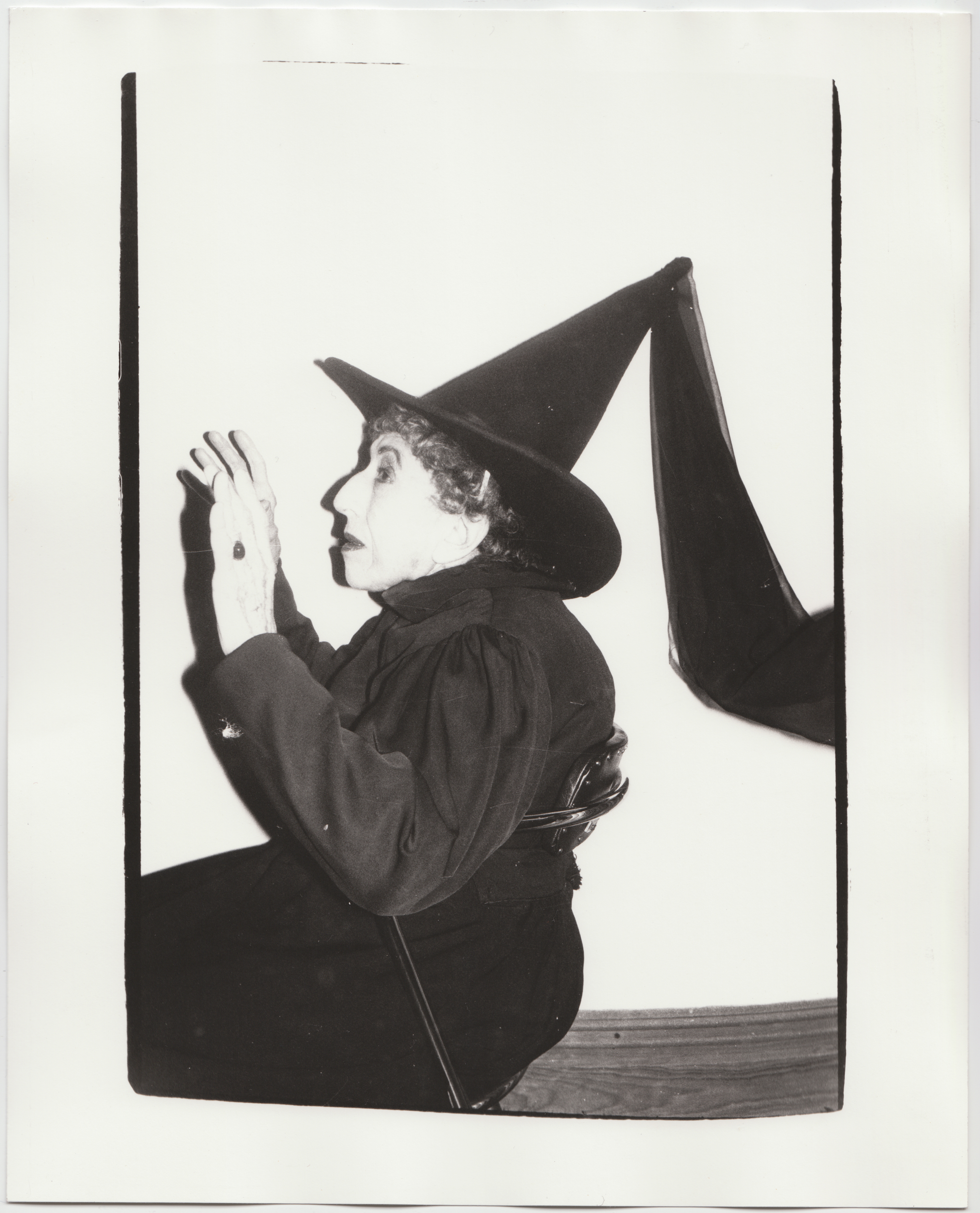 Margaret Hamilton dressed up as a witch with a pointy black hat and fabric flying off of her hat  behind her