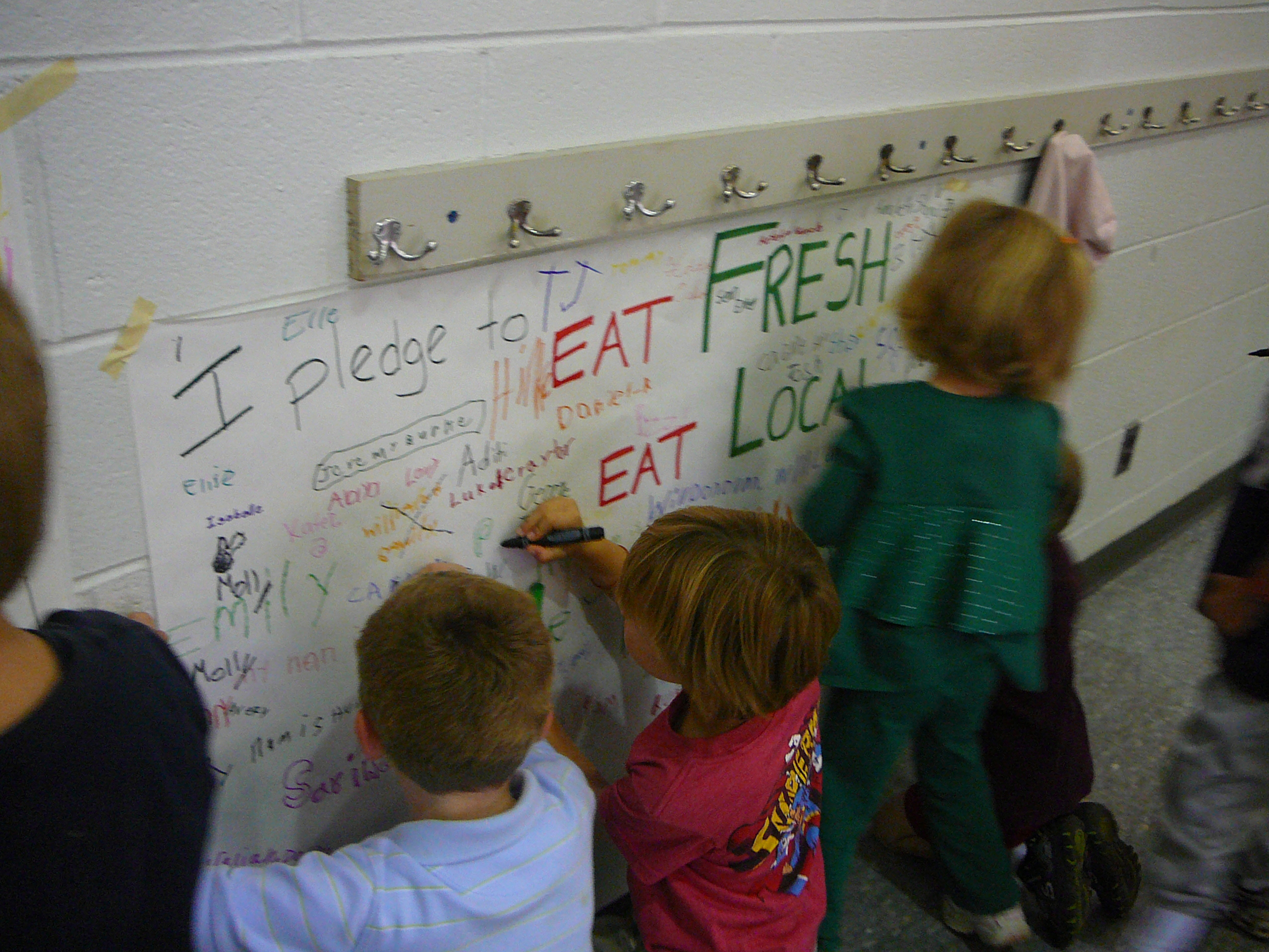 Children writing and drawing on a paper banner that says Eat Fresh