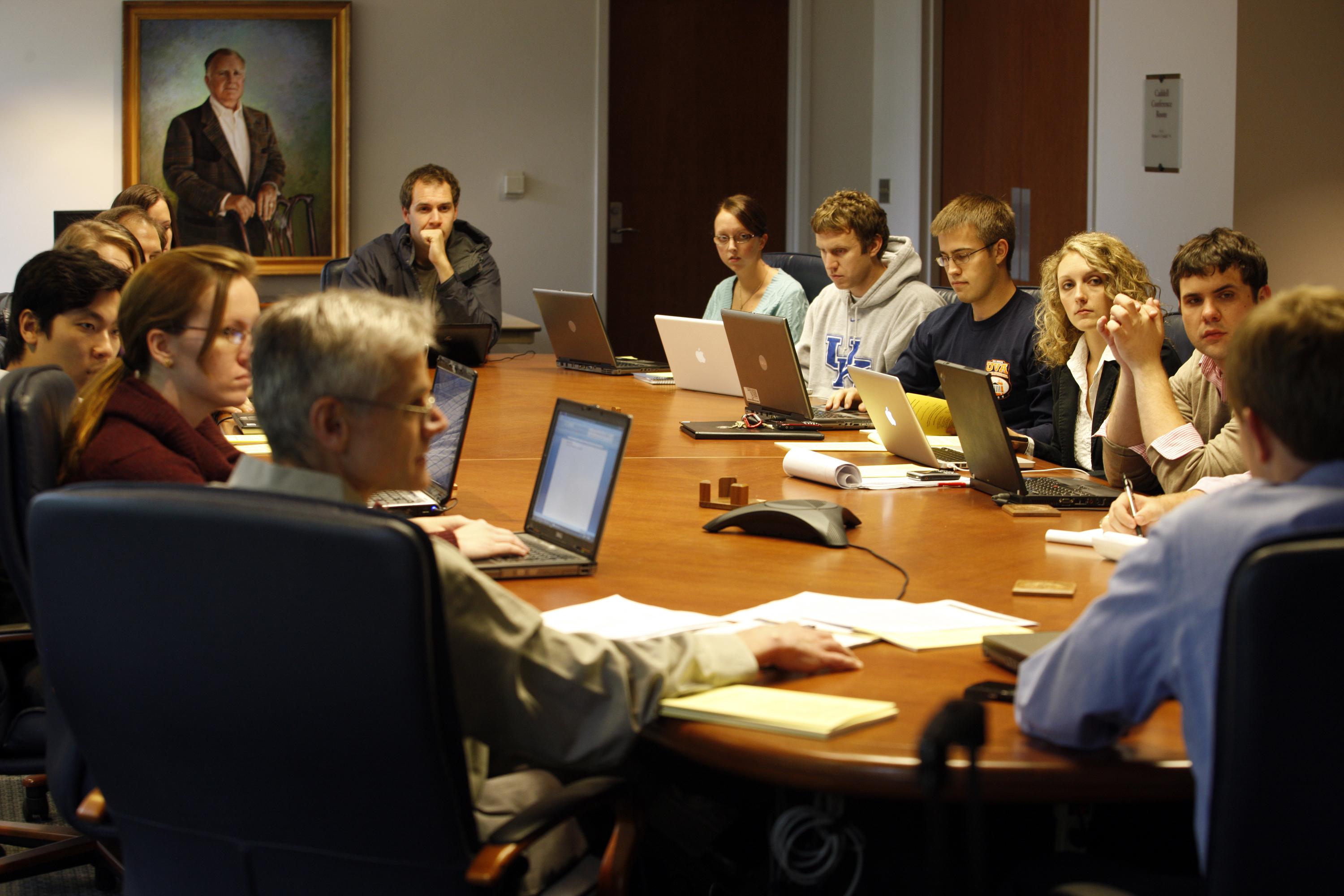 Group of people sitting at an oval table with laptops working together