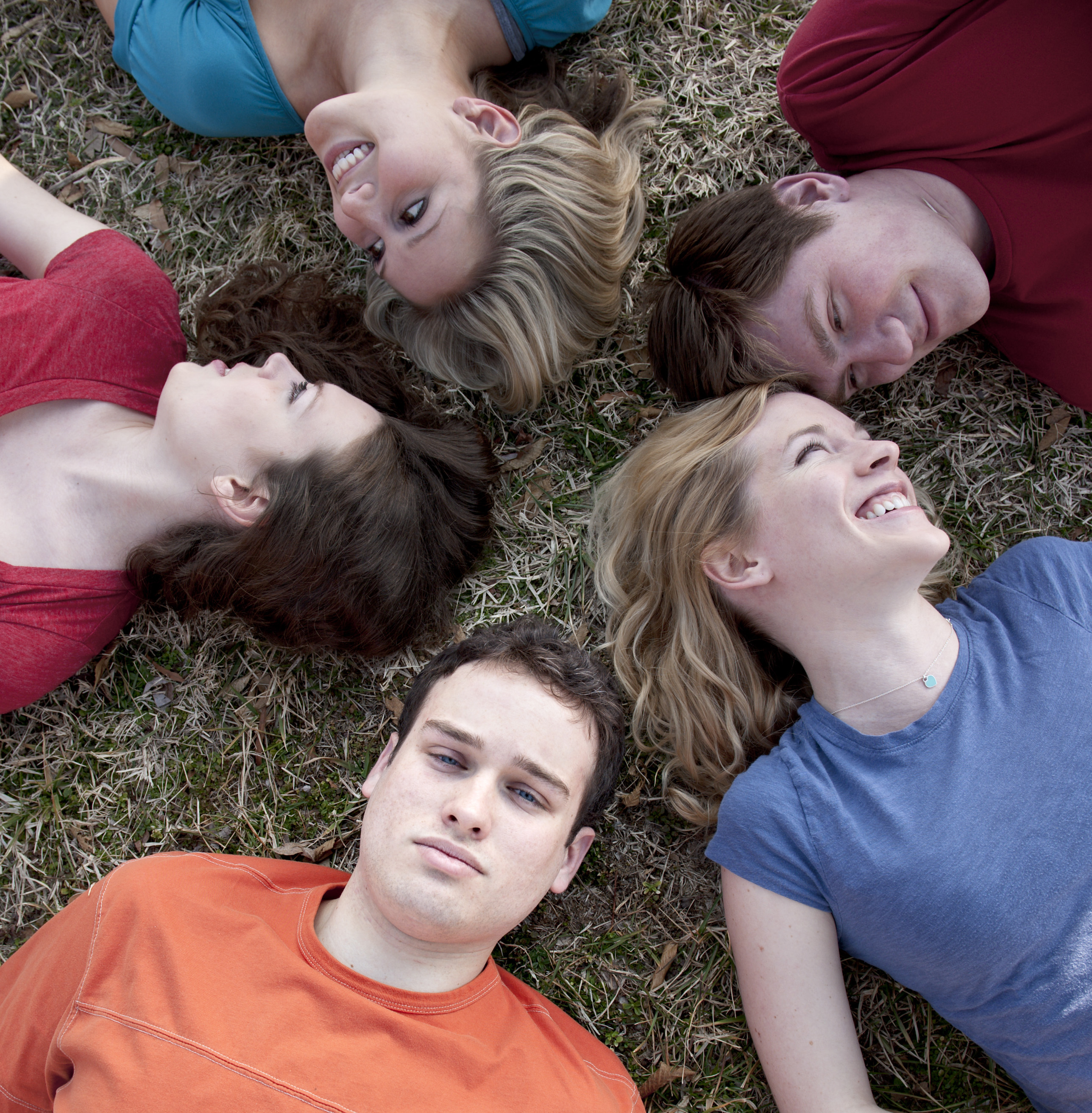 five Students laying on the ground.  Two pairs are looking at each other and the last person is staring directly at the camera