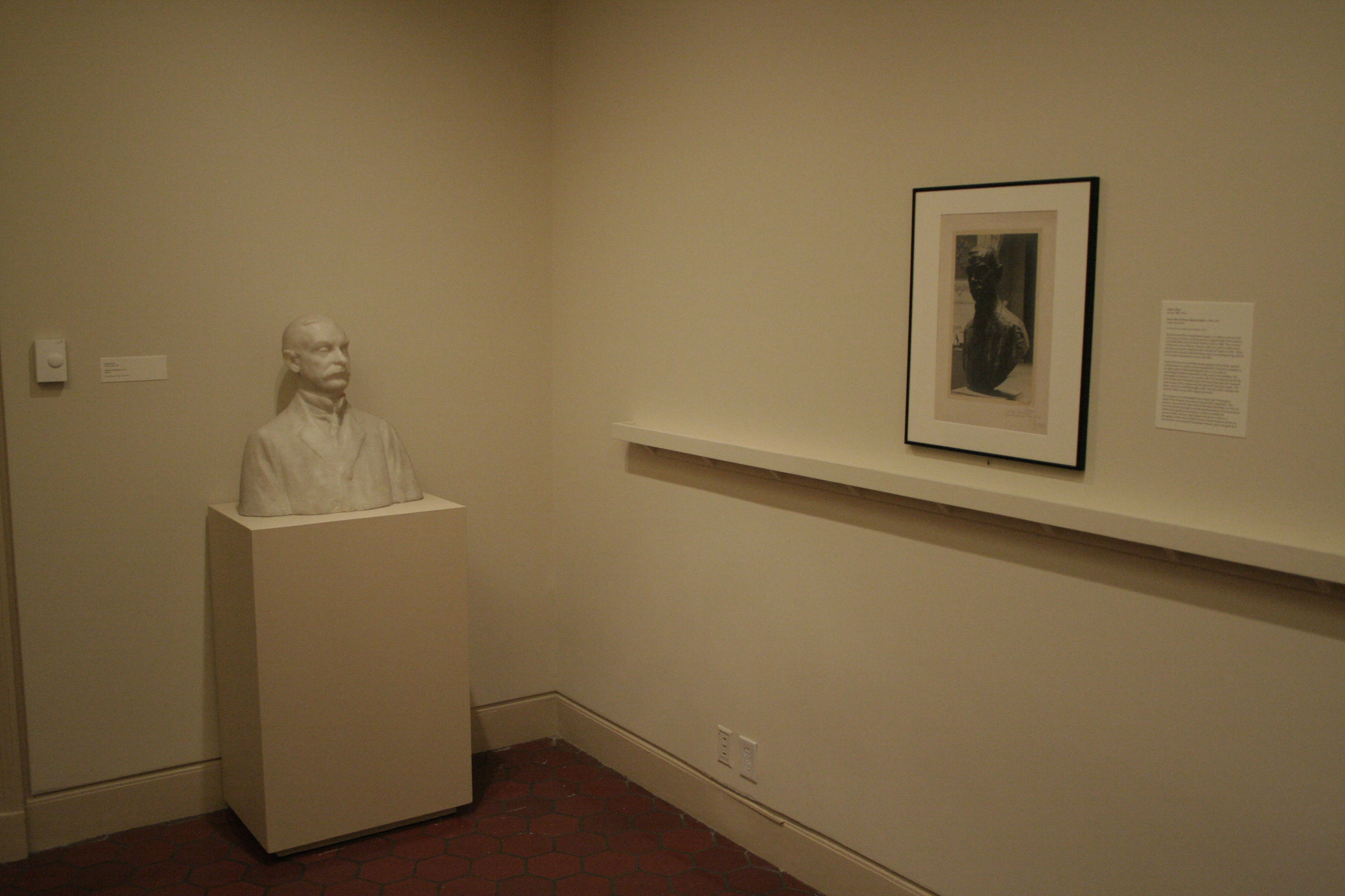 Bust of a man on a pedestal and a picture on a gallery wall