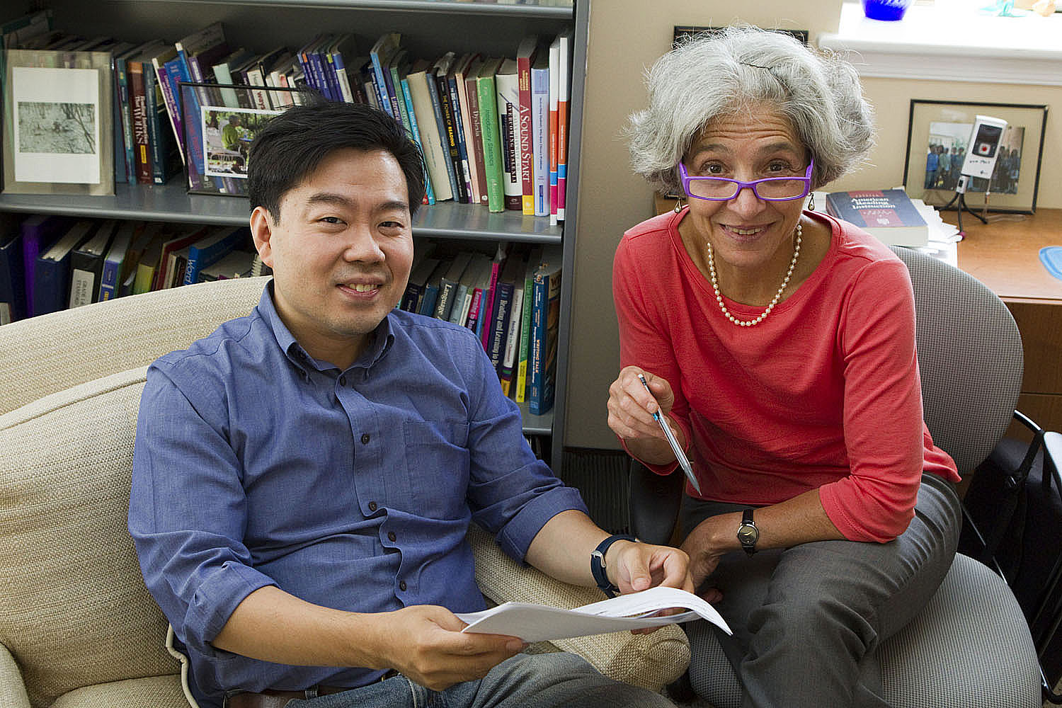 Francis Huang and Marcia Invernizzi sit in chairs working on a paper together look up and smile at the camera