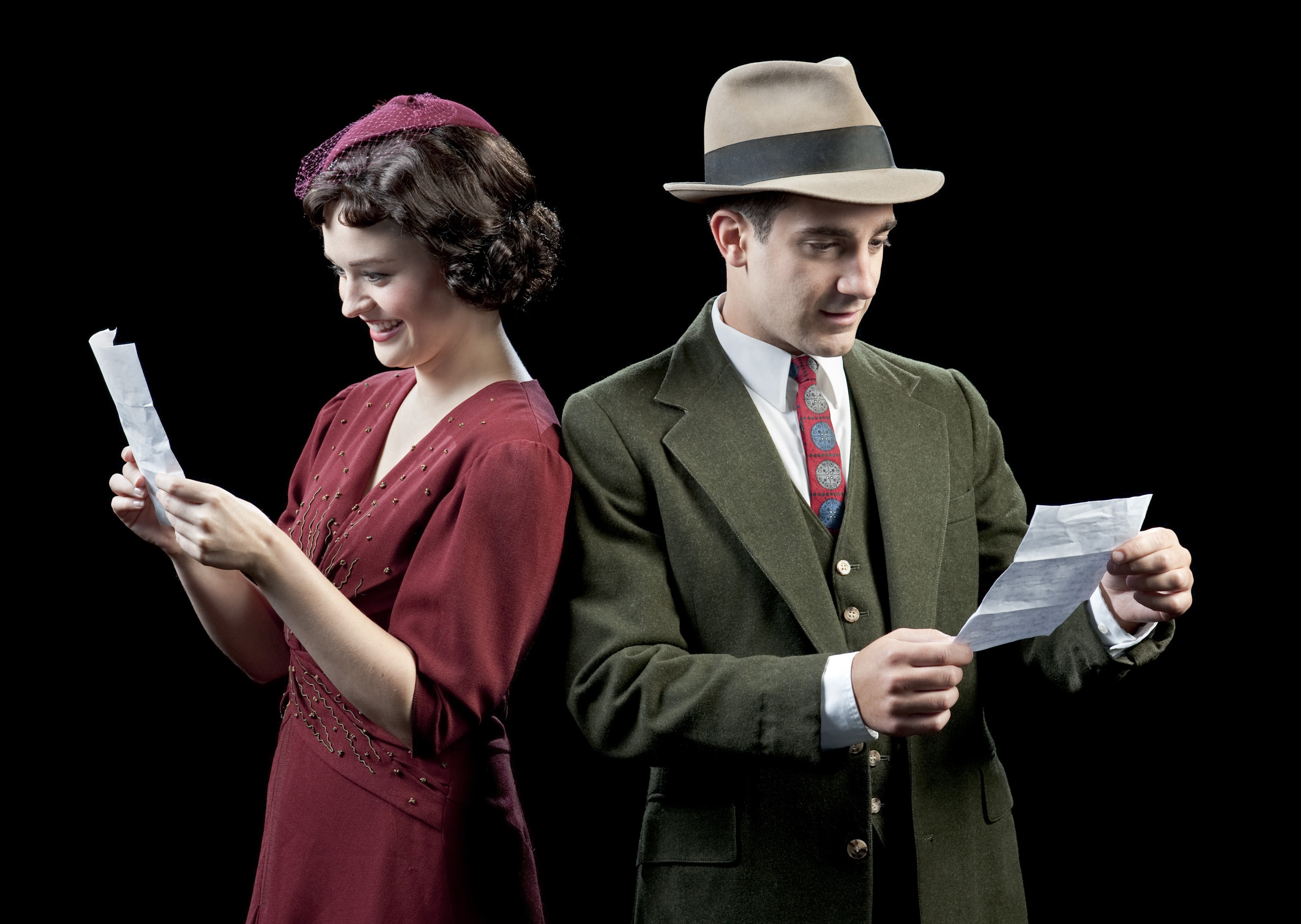Man and woman stand back to back reading love letters dressed in 60's clothing