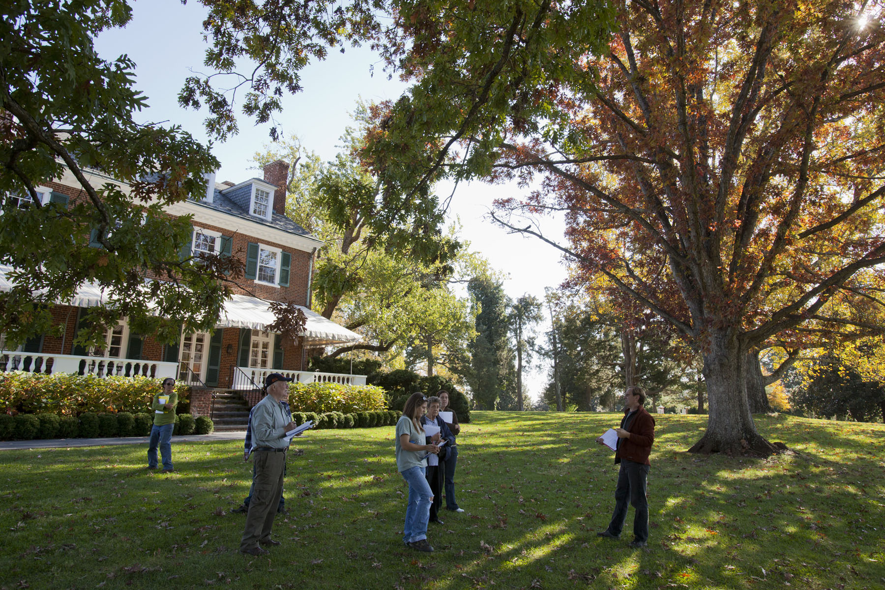 Group of people standing on the lawn in front of a house listening to a tour guide
