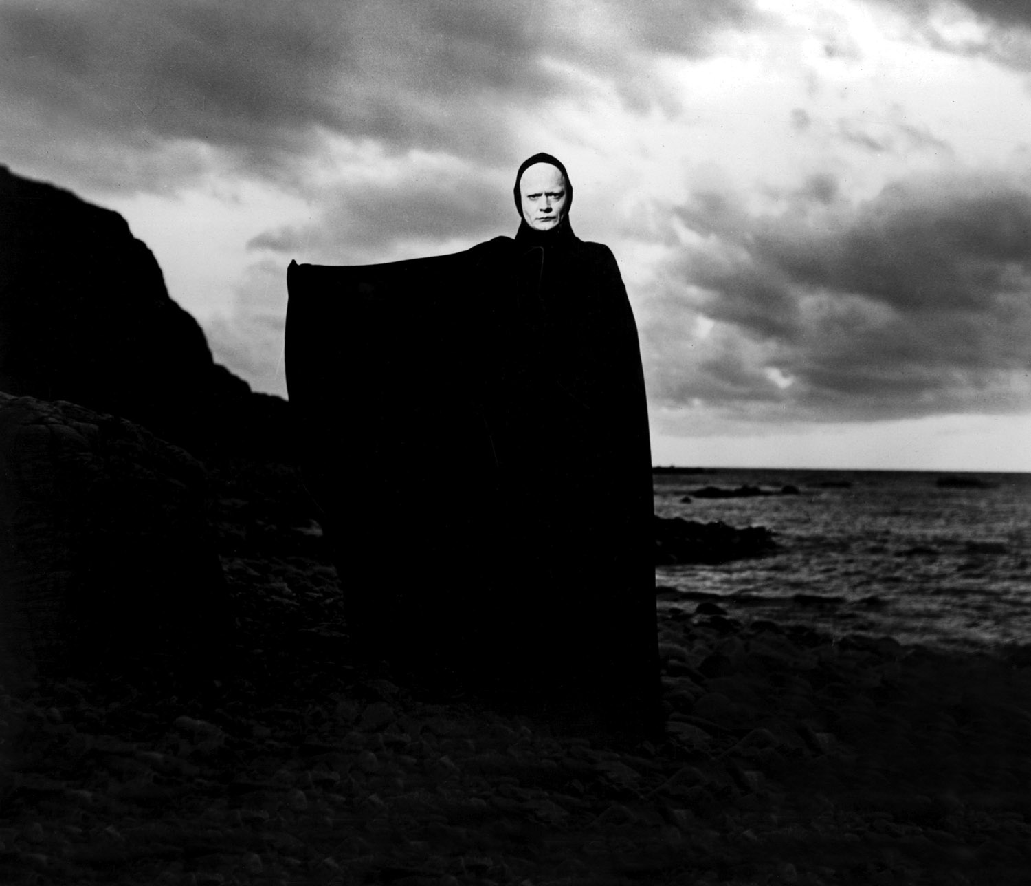 Woman from the The Seventh Seal standing on a cliff in all black holding one arm out to the side