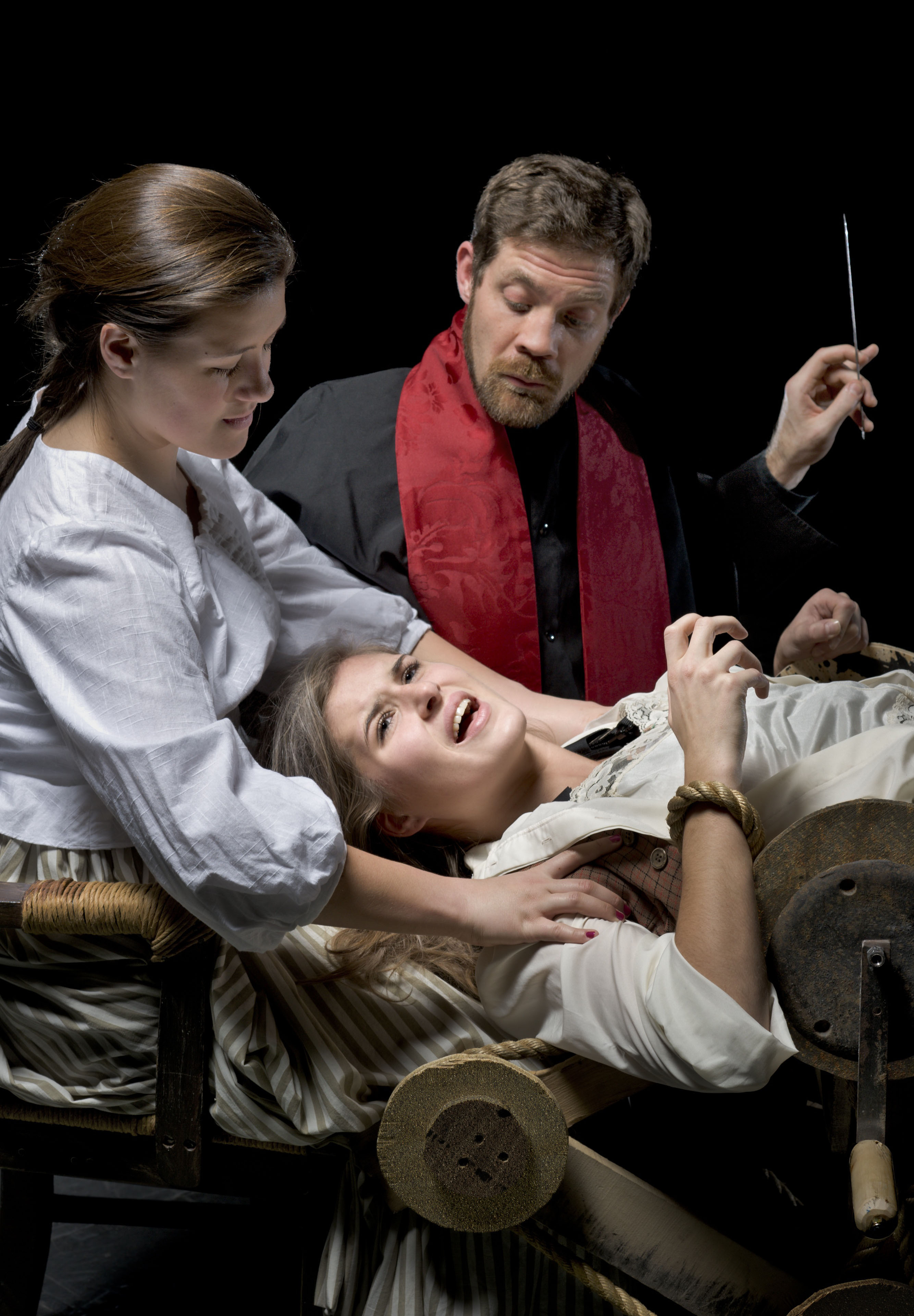Packer (right, Mike Long), assisted by Goody (left, Kyle Hughes), attempts to prove that Joan (center, Anna McQuitty) is a witch during a play