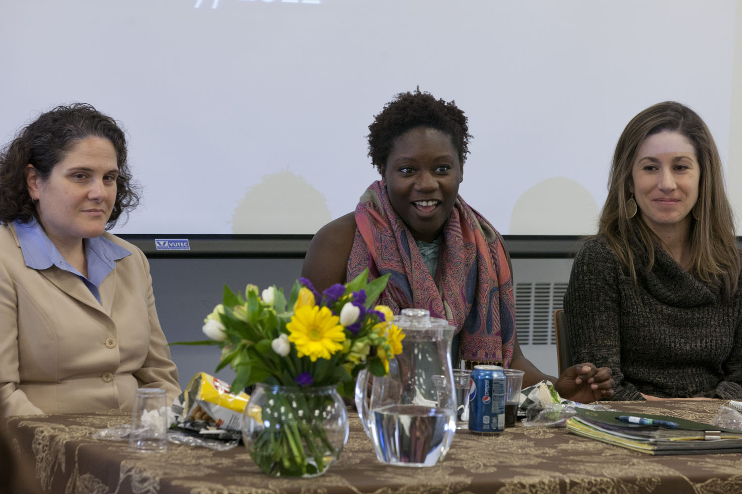 Three alumni sit at a table talking to a crowd.  Left to right: Nicole Eramo, Keiana Mayfield, and Allison Elias