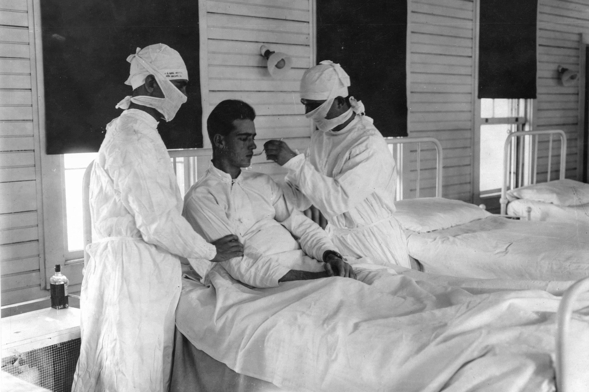 Black and White photo of health care professionals tending to a patient with influenza in a hospital bed