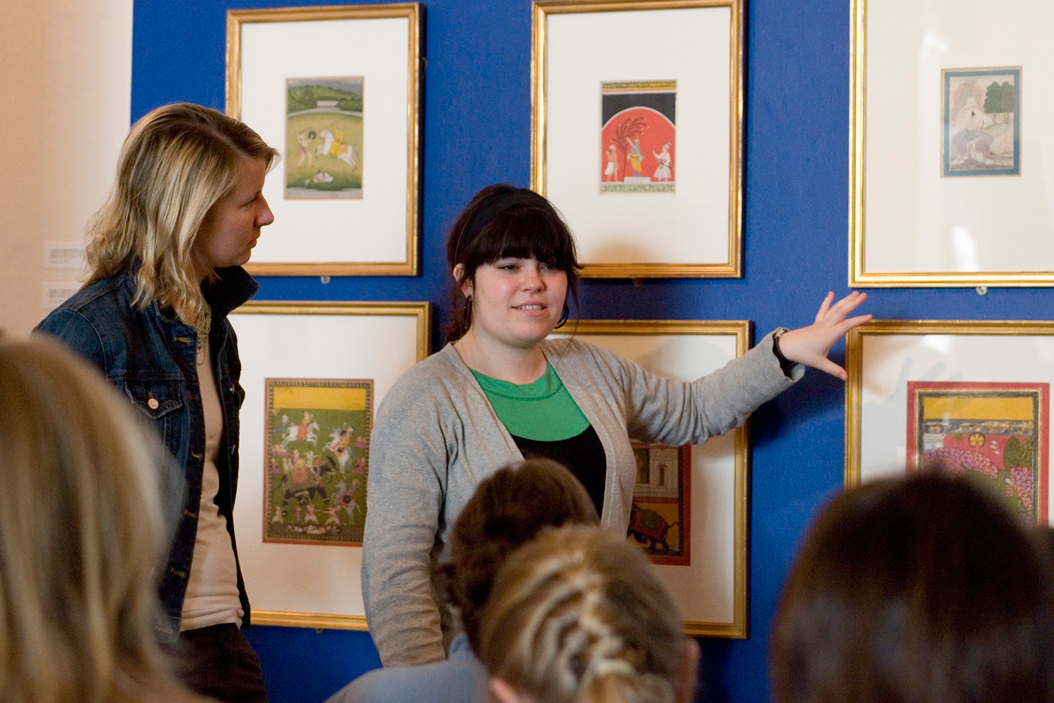 Woman standing and pointing to a painting while talking to a crowd