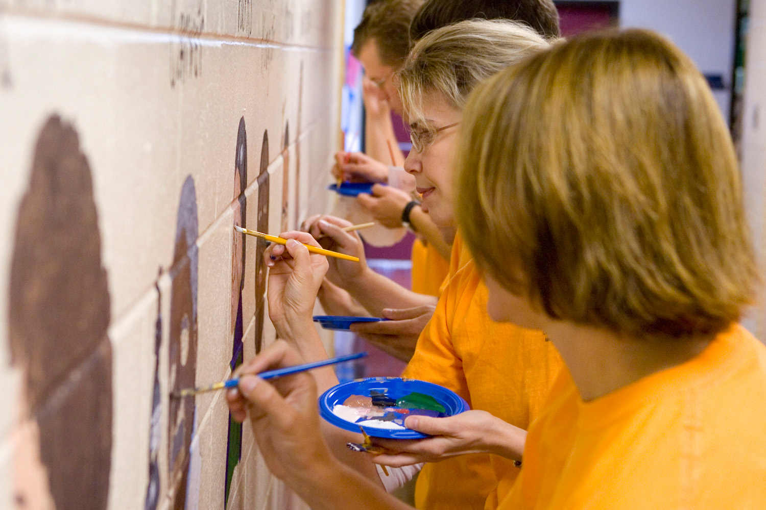 Volunteers painting a mural of famous people on the wall of an elementary school