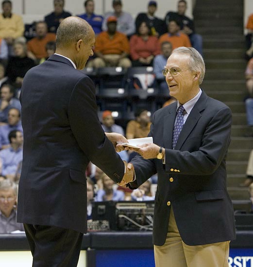 Two men on a basketball court shaking hands and exchanging a piece of paper