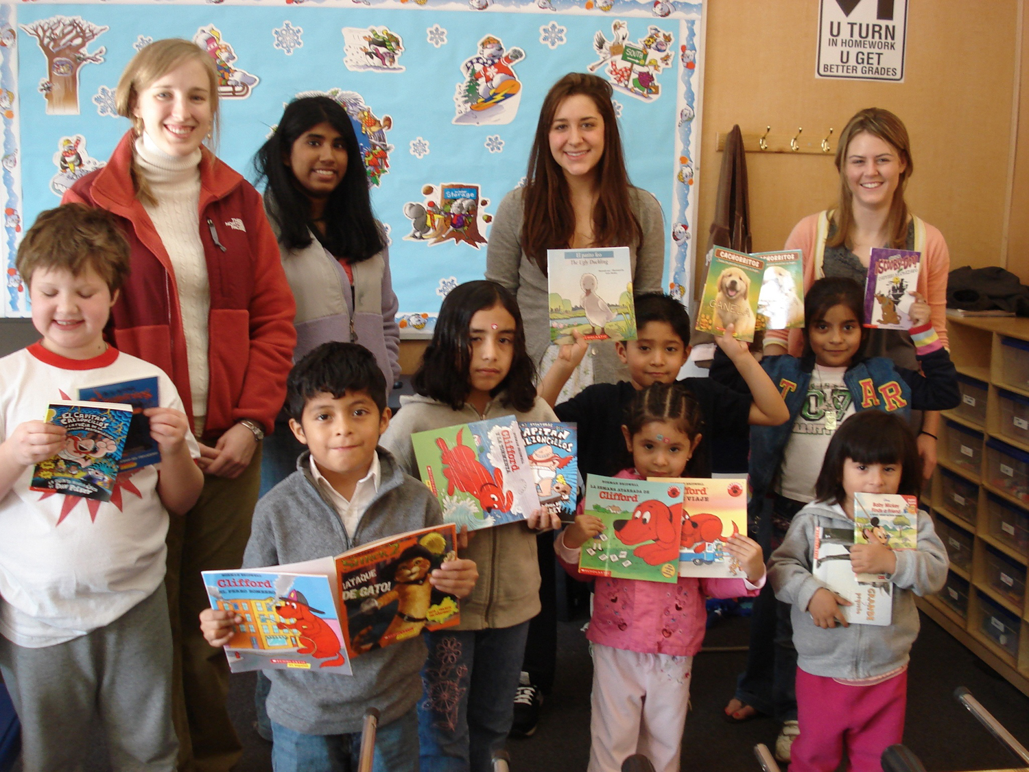 Group photo left to right: Sarah Yates, Priya Komma, Alexandra Hootnick and Claire Kugler stand with a punch of small children holding books