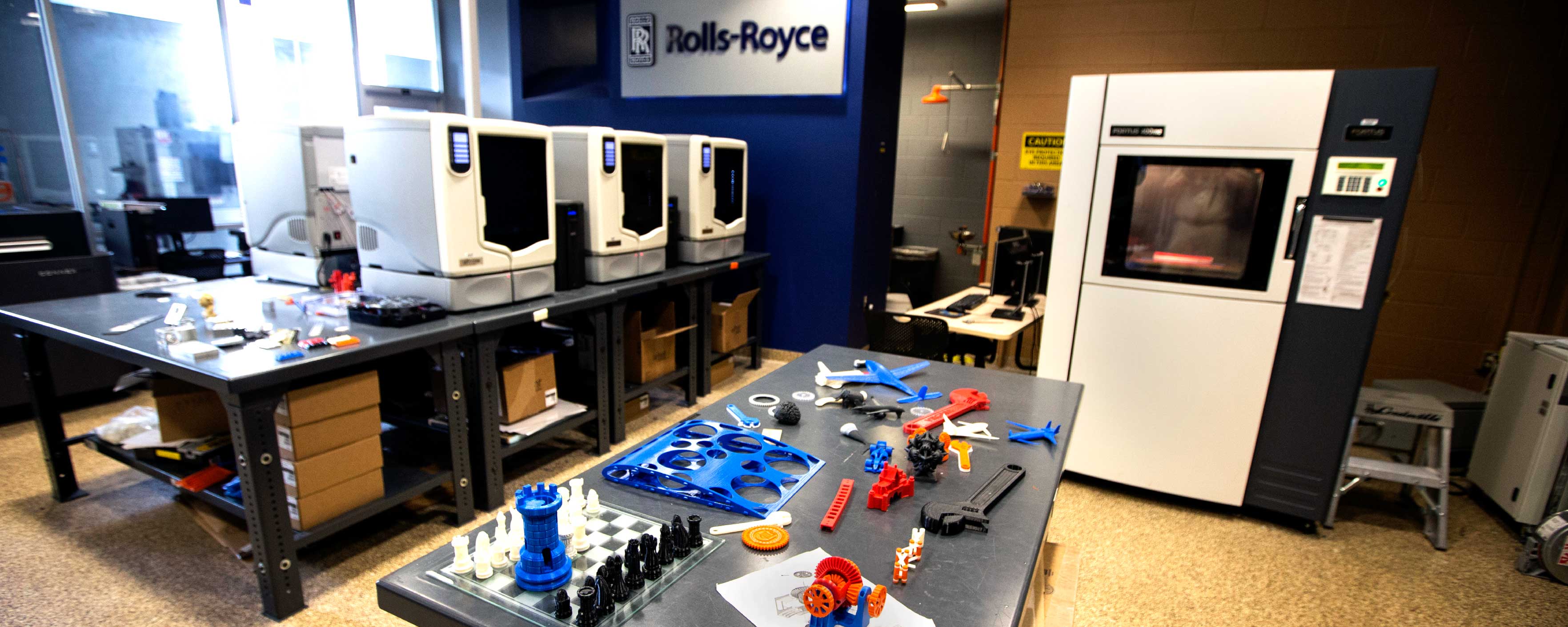 3D printers sitting on a table and 3d creations sitting on another table in the printing lab