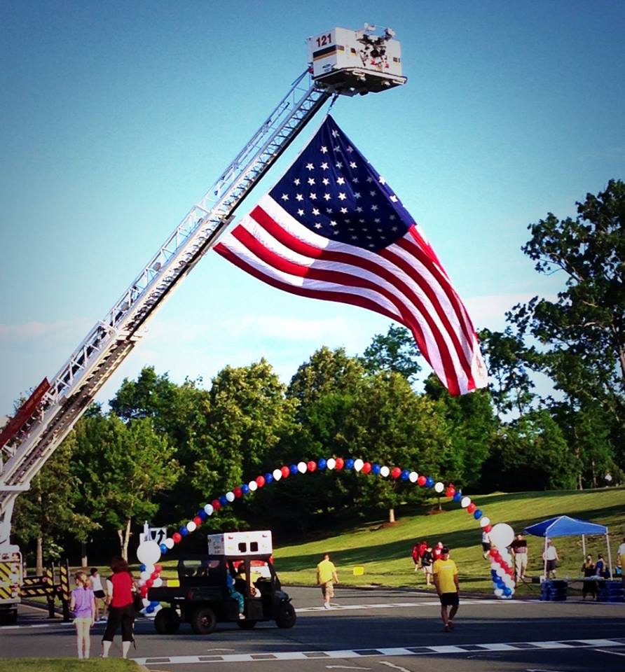 American Flag flying high off of a ladder truck with a red, white, and blue arch