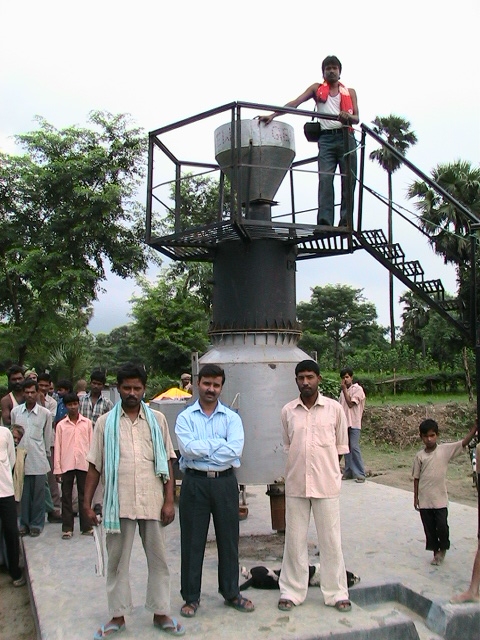 Tamkuha Villagers stand in front of the Husk Power Generator for a group photo