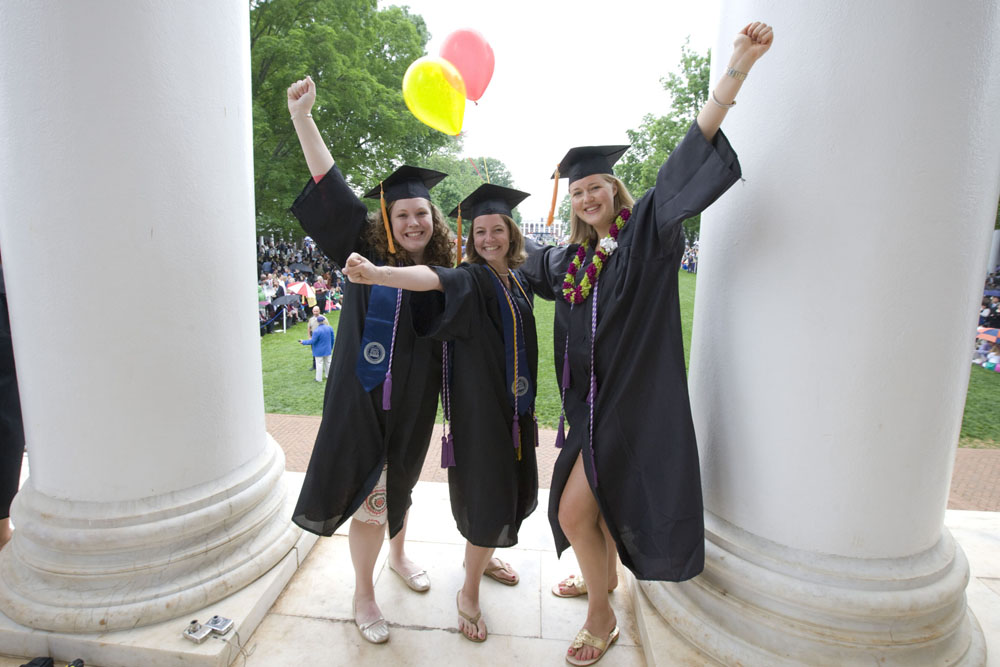 Three graduates lift their arms in excitement between the pillars of the Rotunda