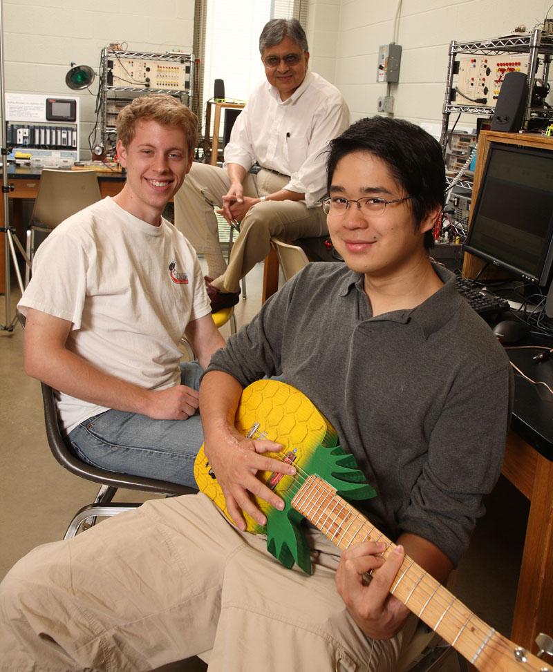 Pradip Sheth watches Will Smith, left, and Patrick Ho play a pineapple guitar