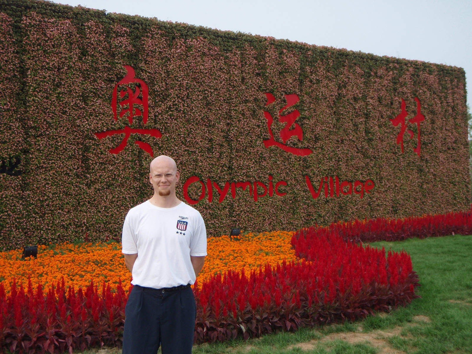 Ian McLeod stands in front of the olympic Village sign