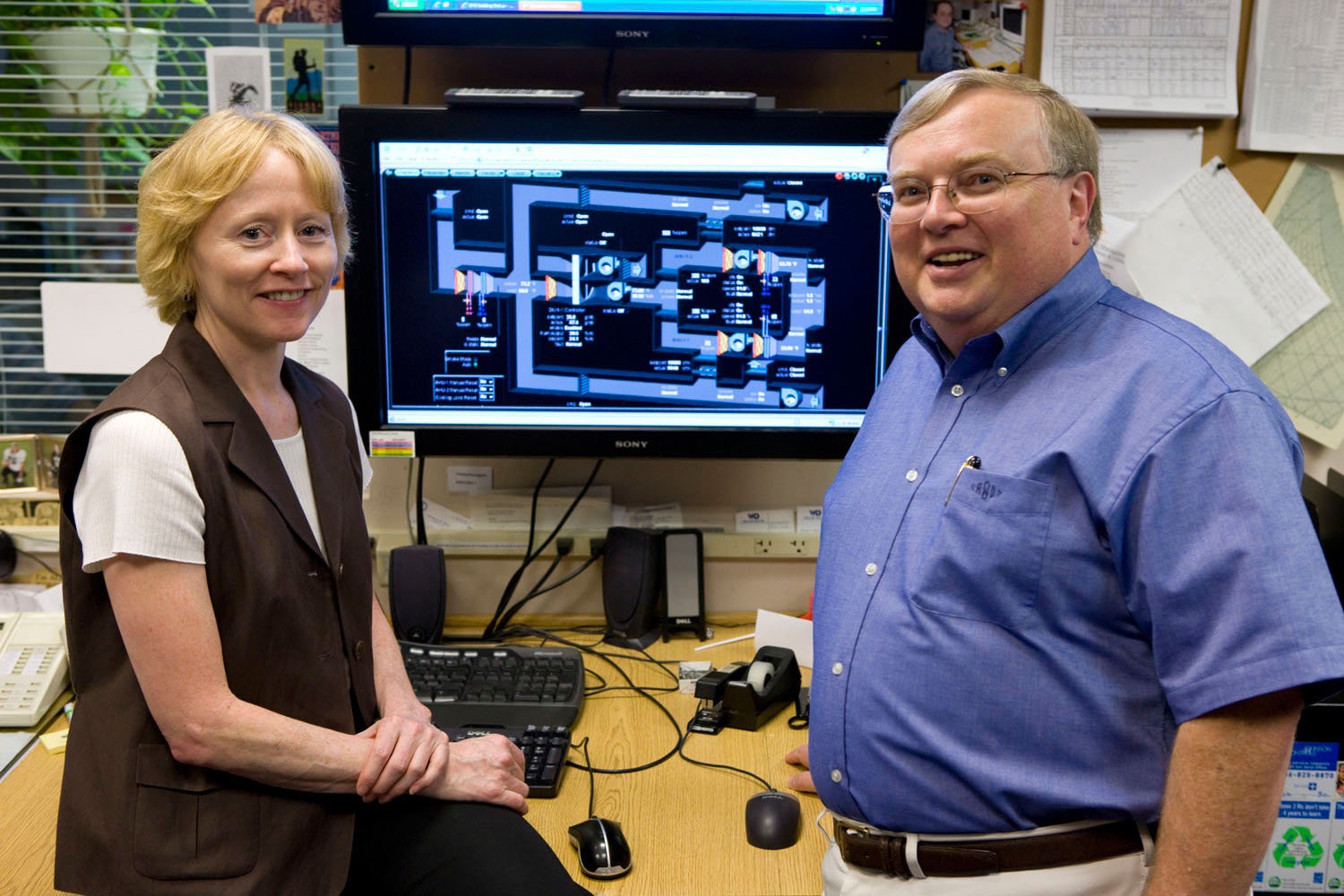 Cheryl Gomez (left) and Ron Williams stand in front of a computer smiling at the camera