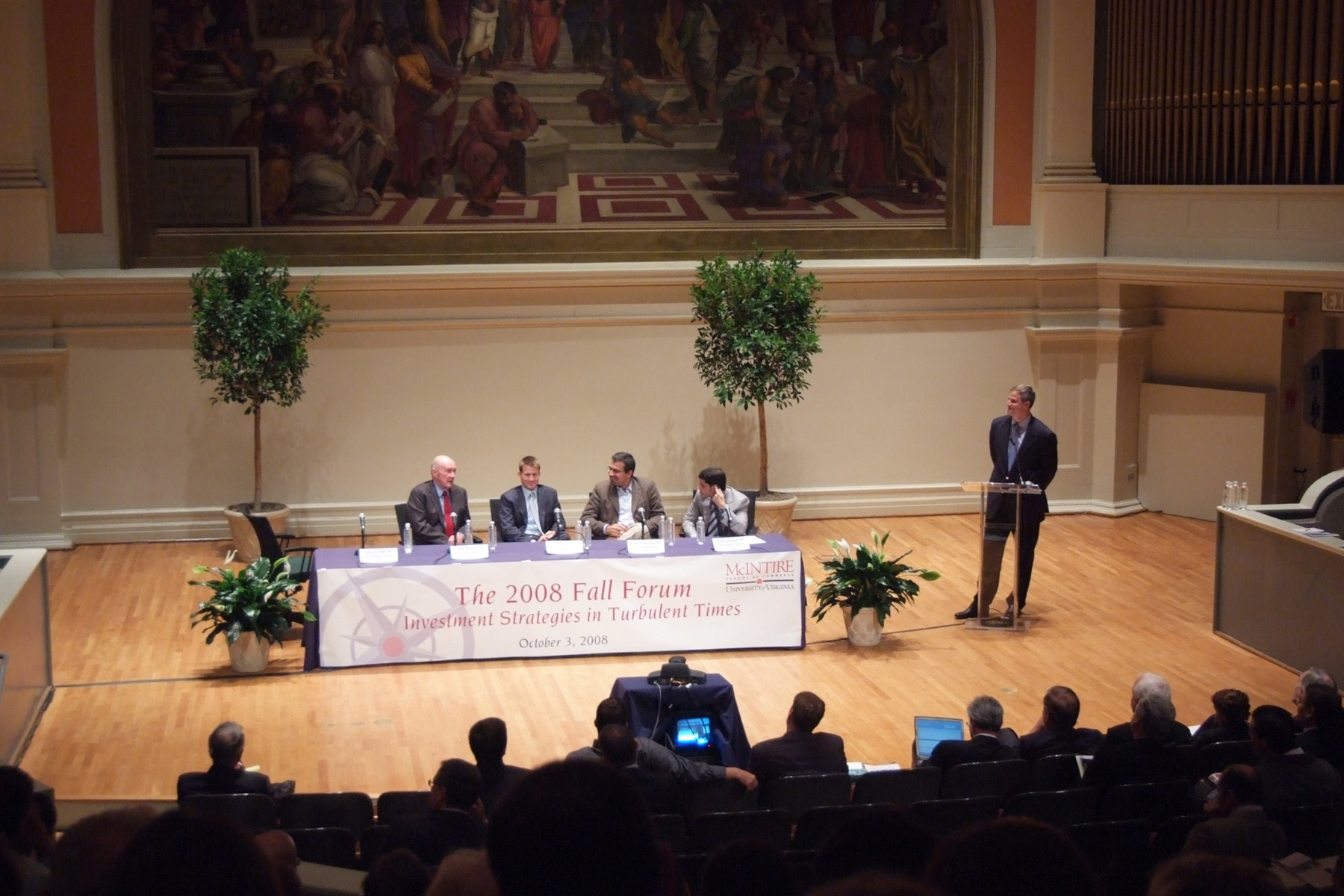 Panelists sitting at a table while a moderator stands at a podium